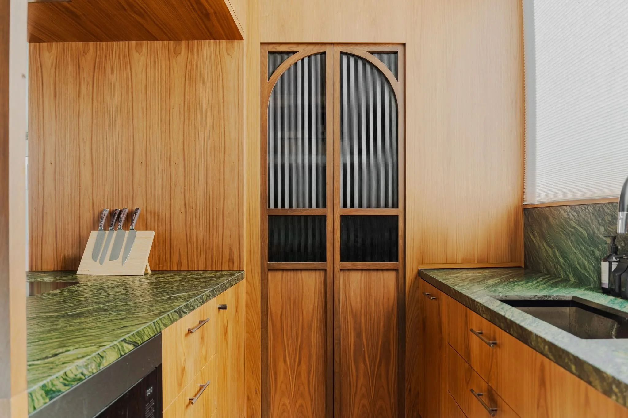 Kitchen with wooden cabinets, green marble countertops, a knife holder with four knives, and a sliding door with glass panels.