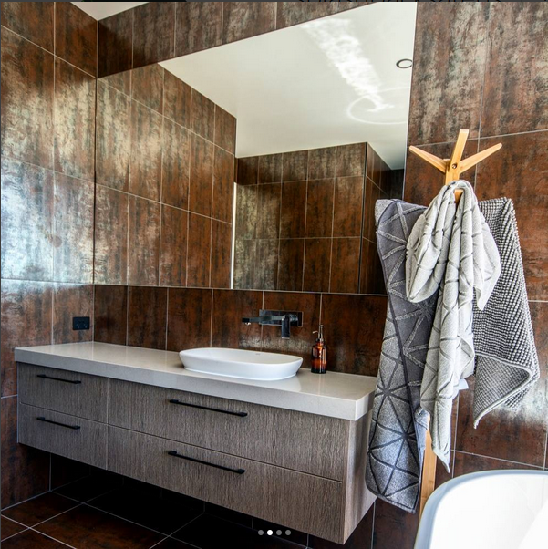 Modern bathroom with brown tiled walls, a large mirror, a floating vanity with a vessel sink, and towels hanging on a wooden towel rack.