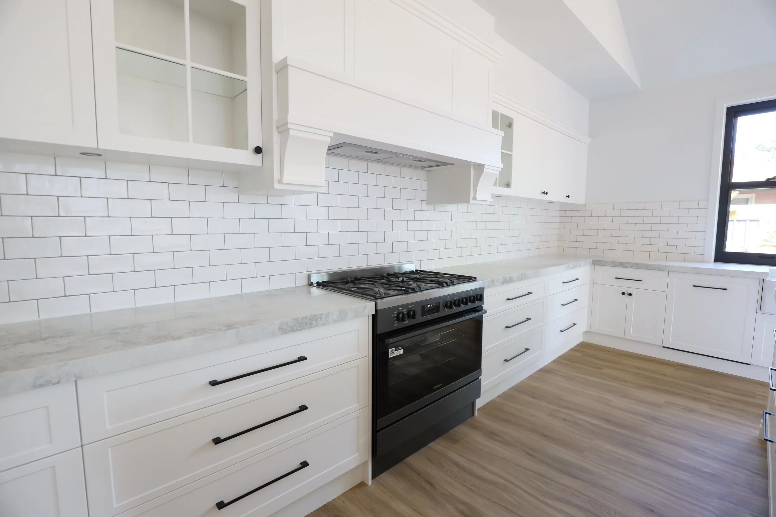 Modern white kitchen with black hardware, white subway tile backsplash, black oven, and wood flooring.