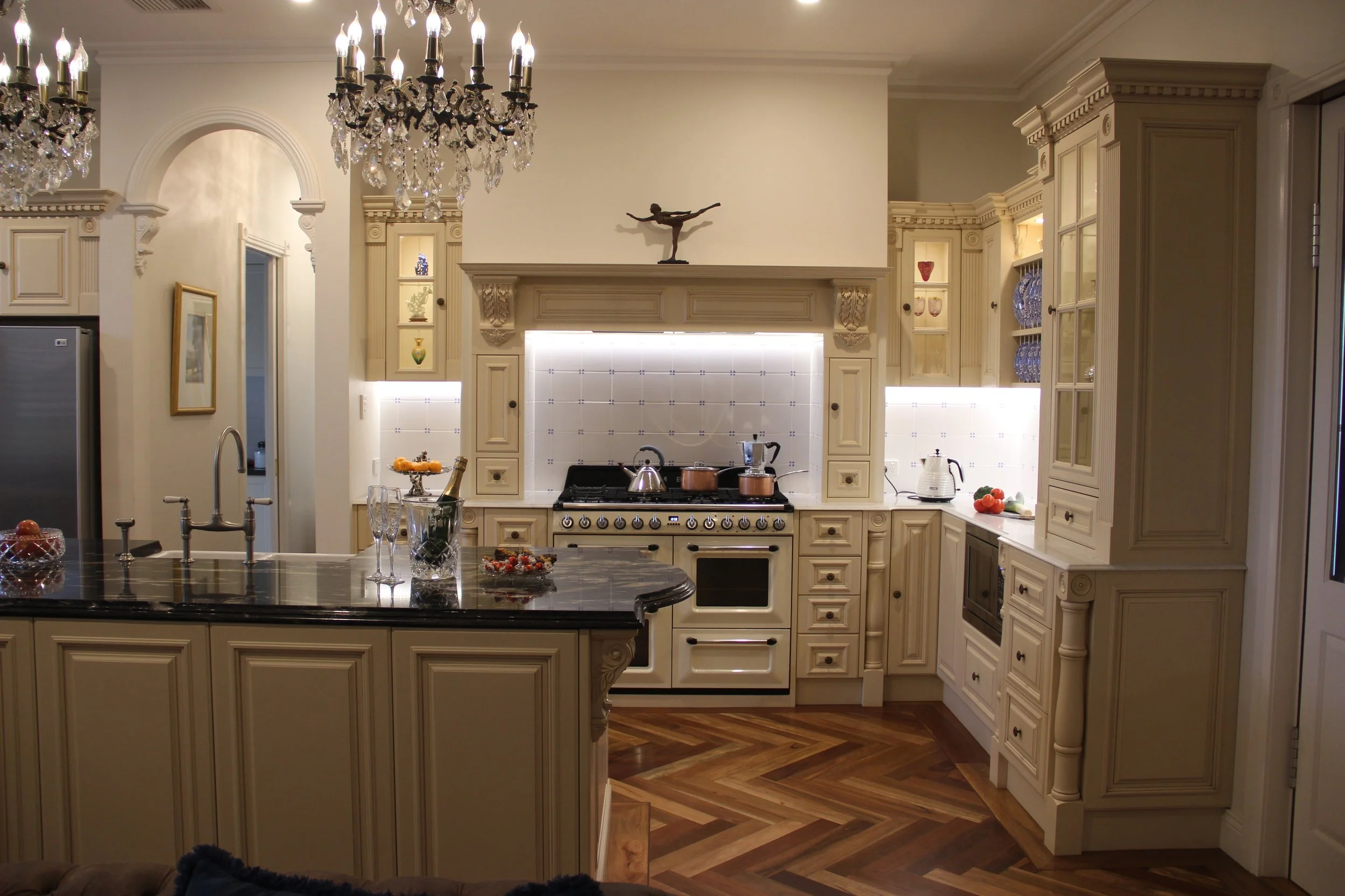 Elegant kitchen with cream-colored cabinets, black marble island, chandeliers, and hardwood floors.