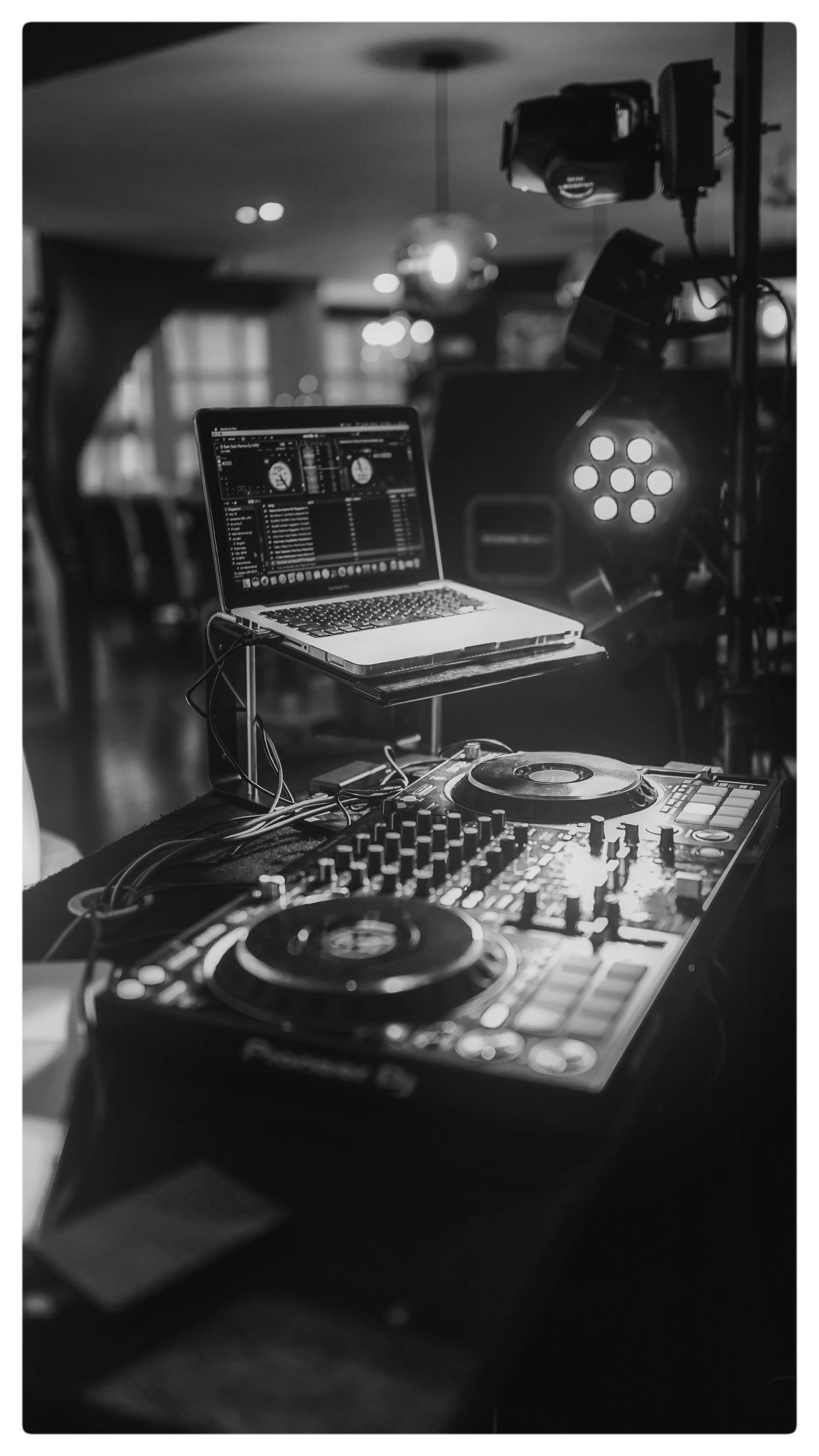 DJ equipment set up with a laptop, turntables, and mixer in a dimly lit venue, possibly for a live music or DJ event.