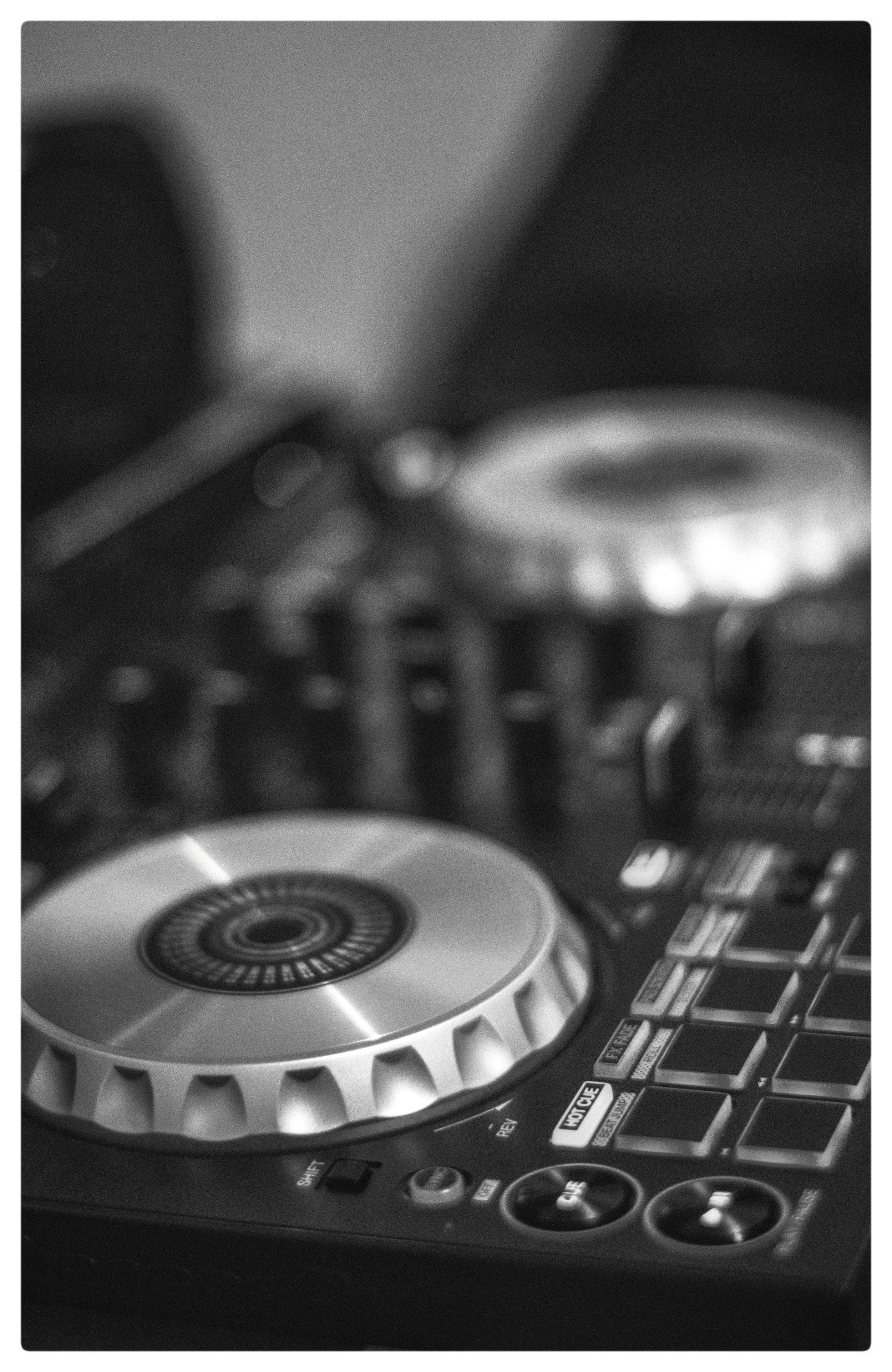 Close-up of DJ controller with jog wheel, buttons, and knobs, in black and white.