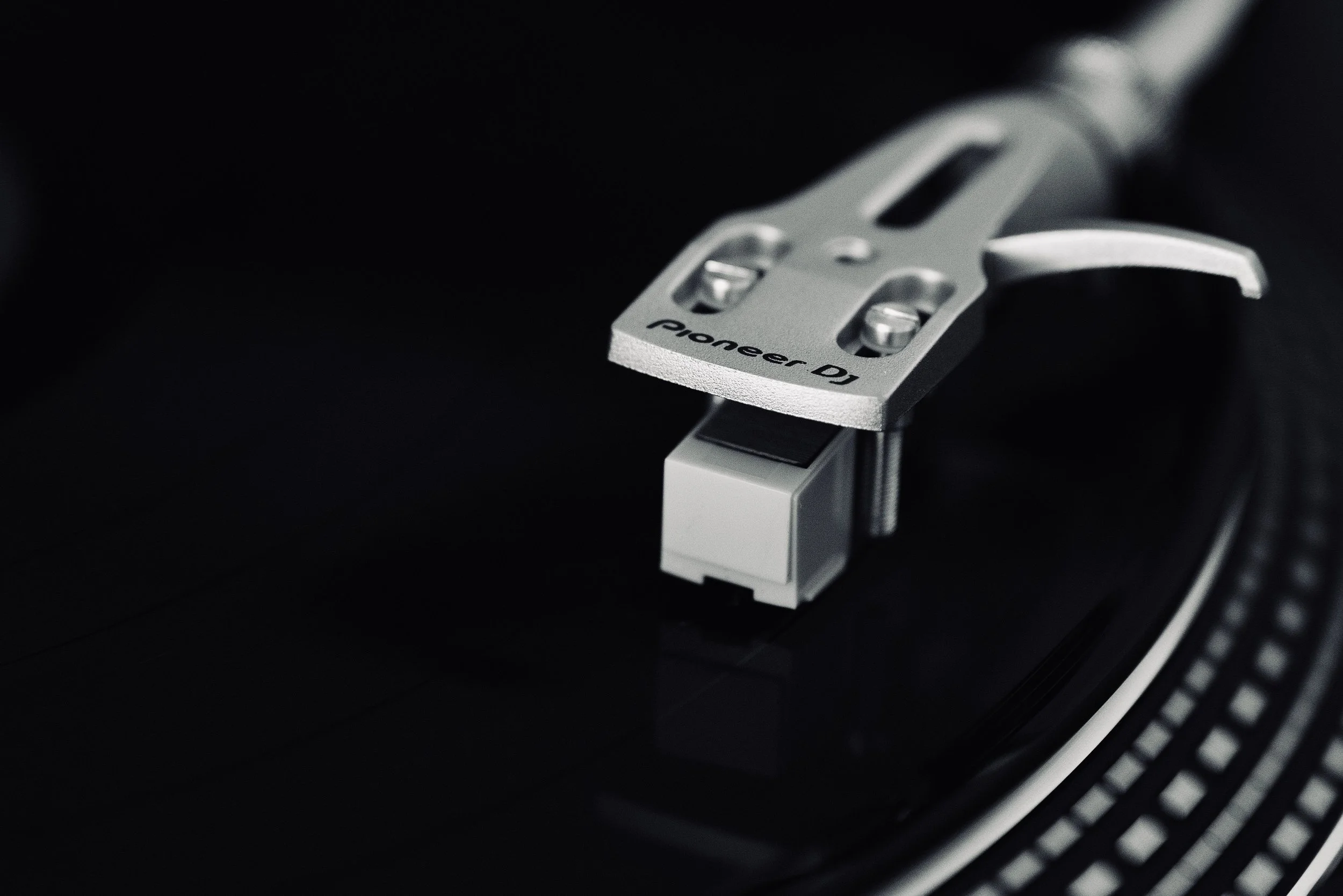 Close-up of a Pioneer DJ turntable's tonearm with black background.