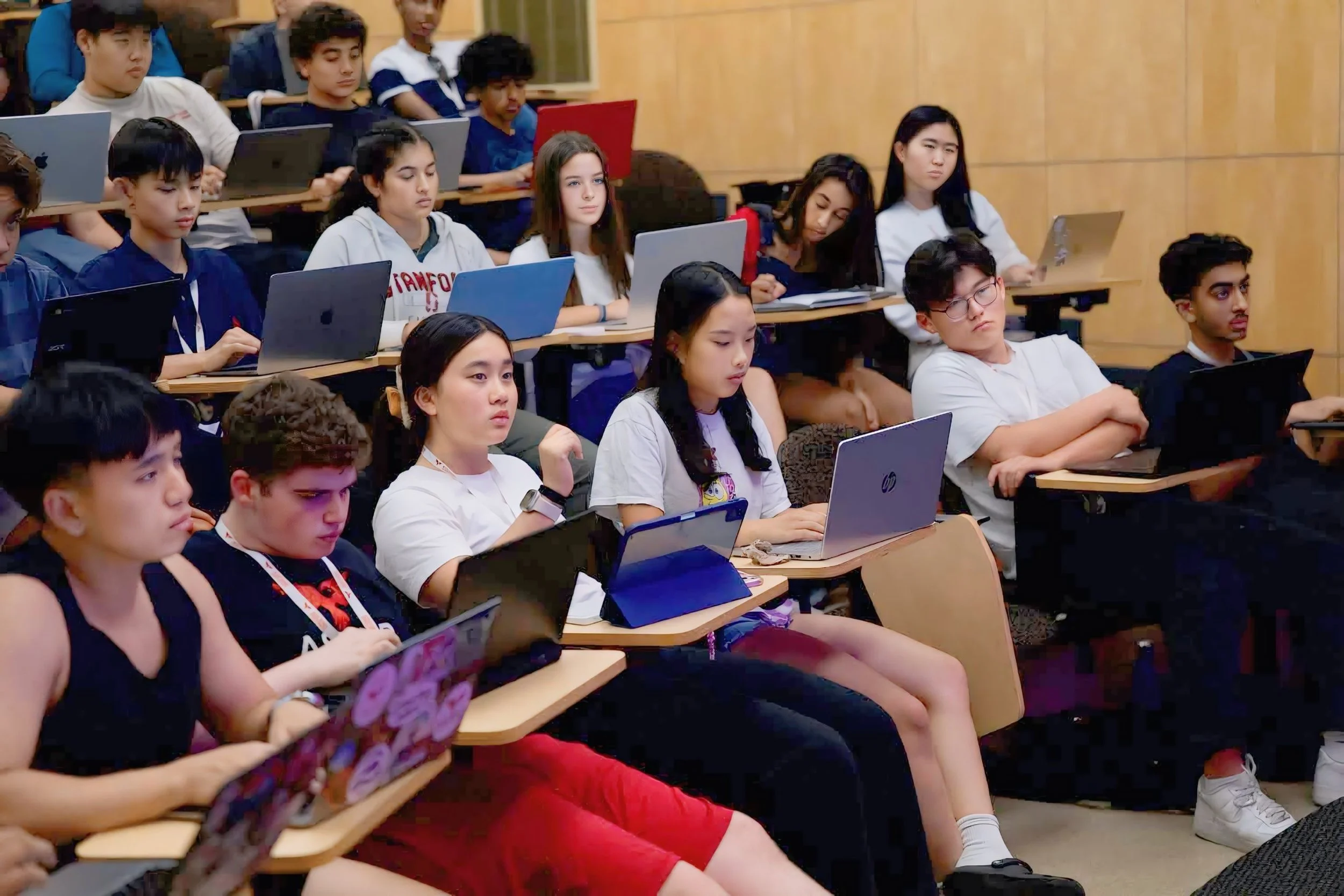 Students sitting in a classroom with laptops, focused on a lecture or presentation.