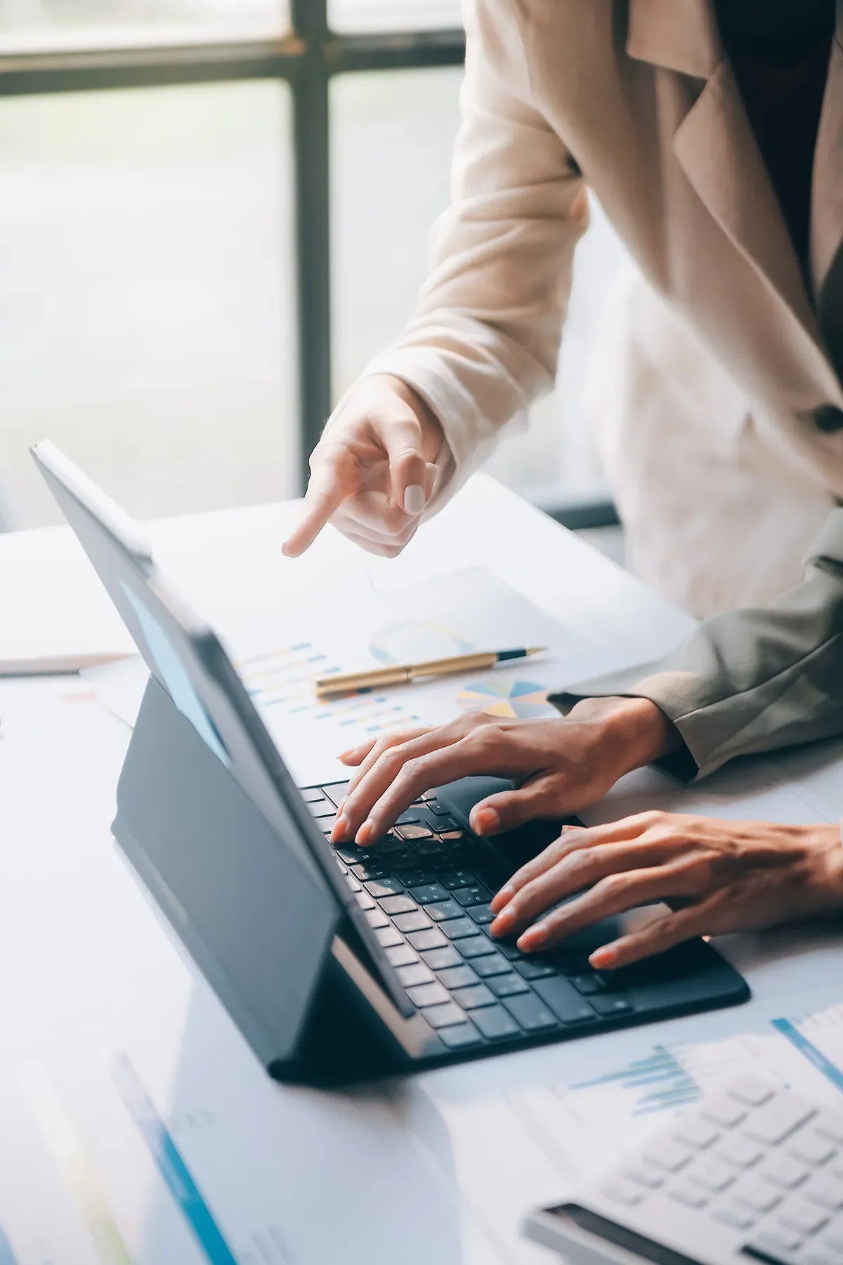 Two individuals working together at a desk with a laptop and documents containing charts and graphs.