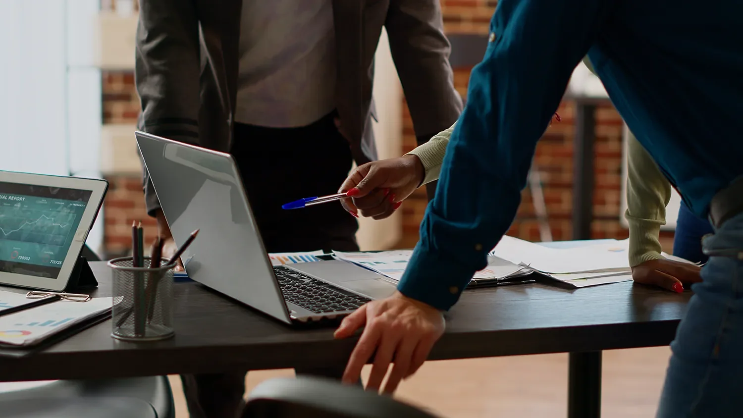 Businesspeople review data and graphs on laptops and papers during a meeting in an office.