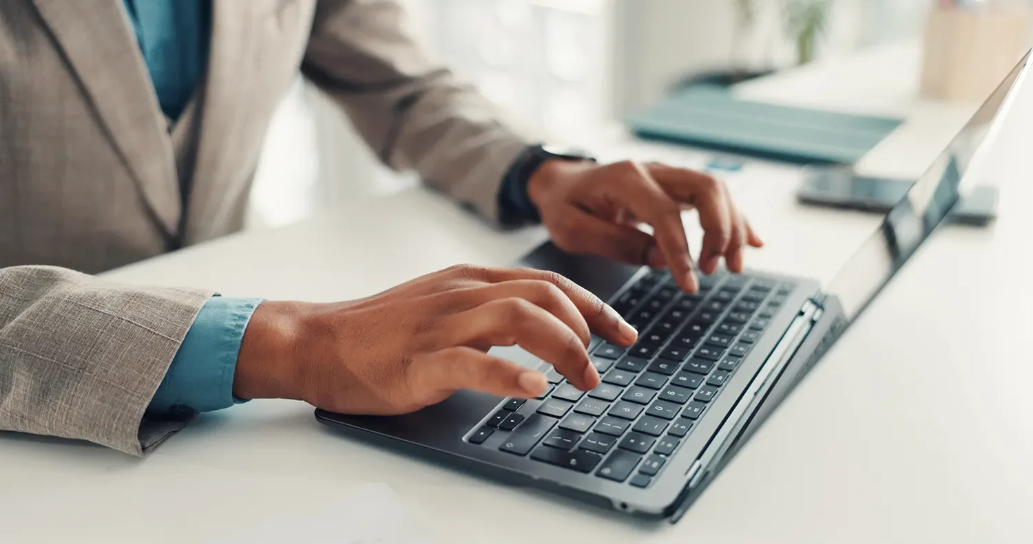 Person typing on a laptop keyboard at a white desk.