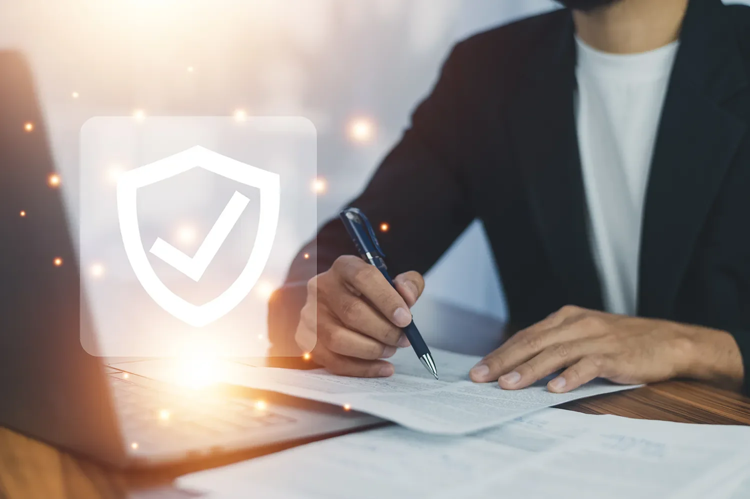 Person in a suit signing documents at a desk, with a shield icon and checkmark overlay representing security.