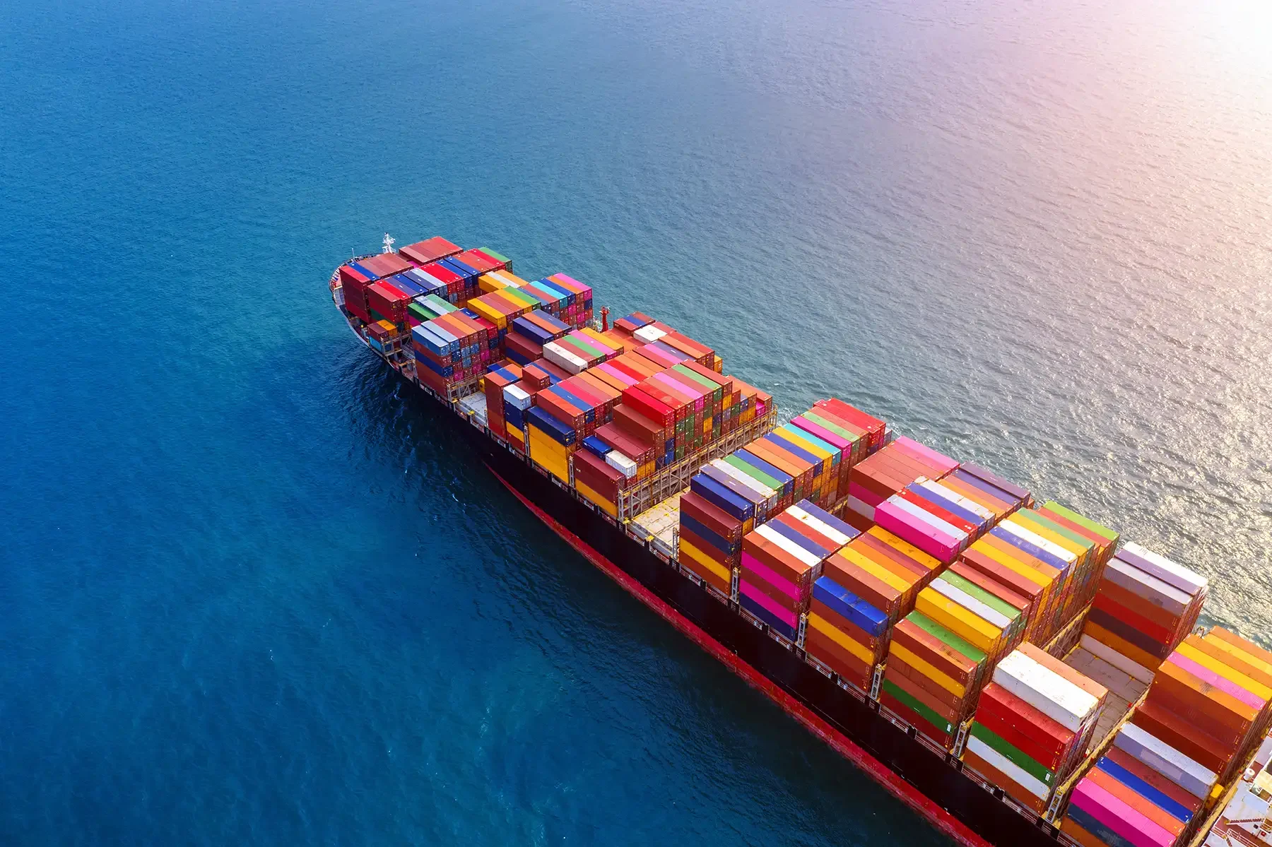 A large cargo ship sailing through the ocean carrying numerous colorful shipping containers.