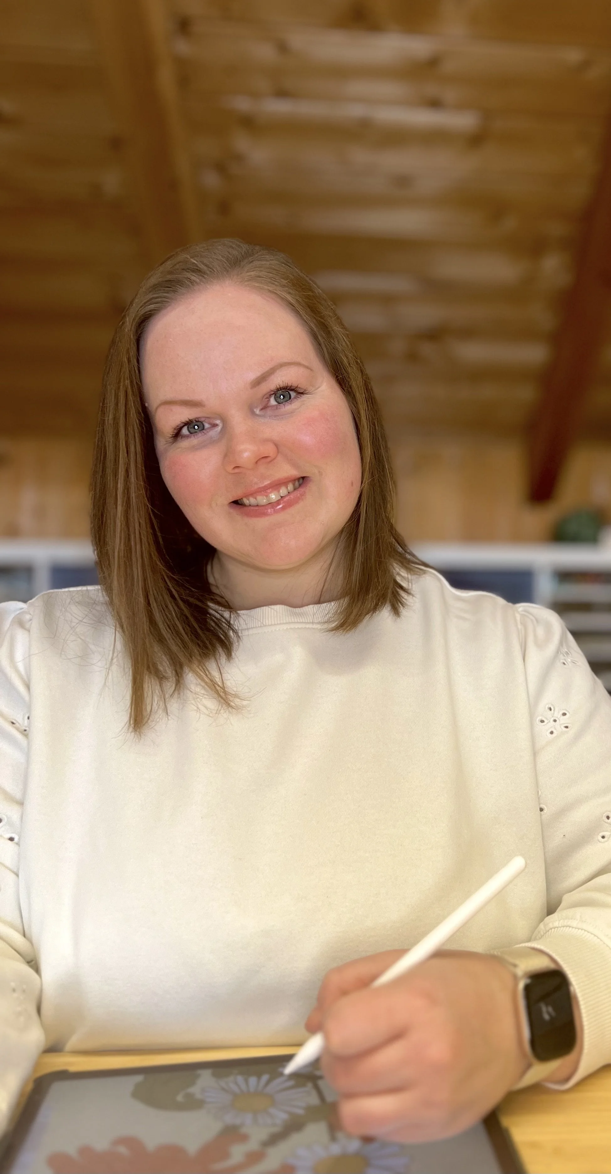 Eine lachende Frau mit braunen Haaren, die mit einem Touchscreen-Tablet arbeitet, in einem Raum mit Holzdecke.