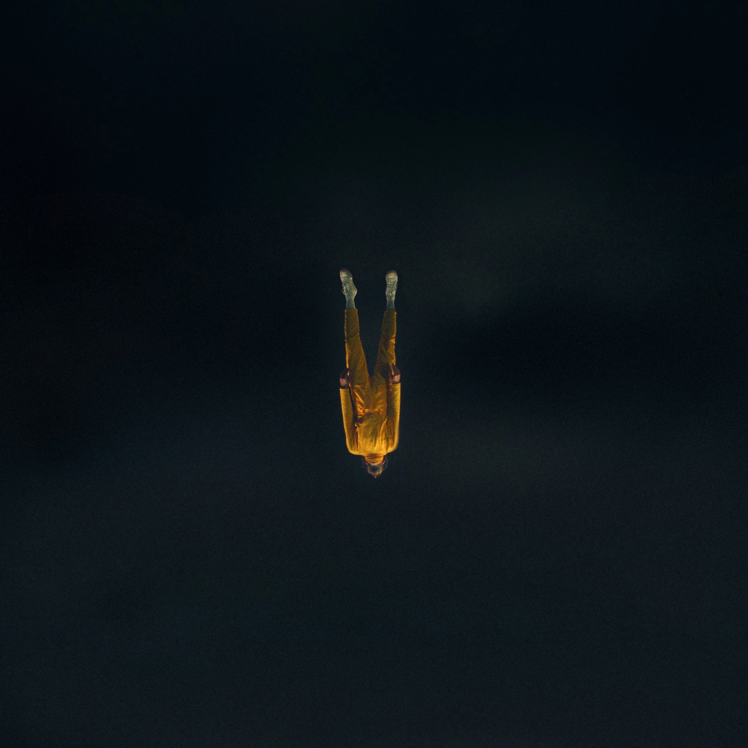 A person in an orange jumpsuit and white shoes standing upside down, reflected on a dark, possibly wet, surface.