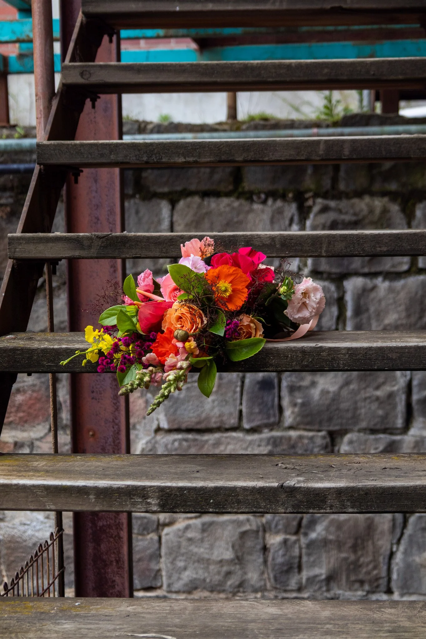 A colorful flower bouquet resting on a set of outdoor wooden stairs with a stone wall background.