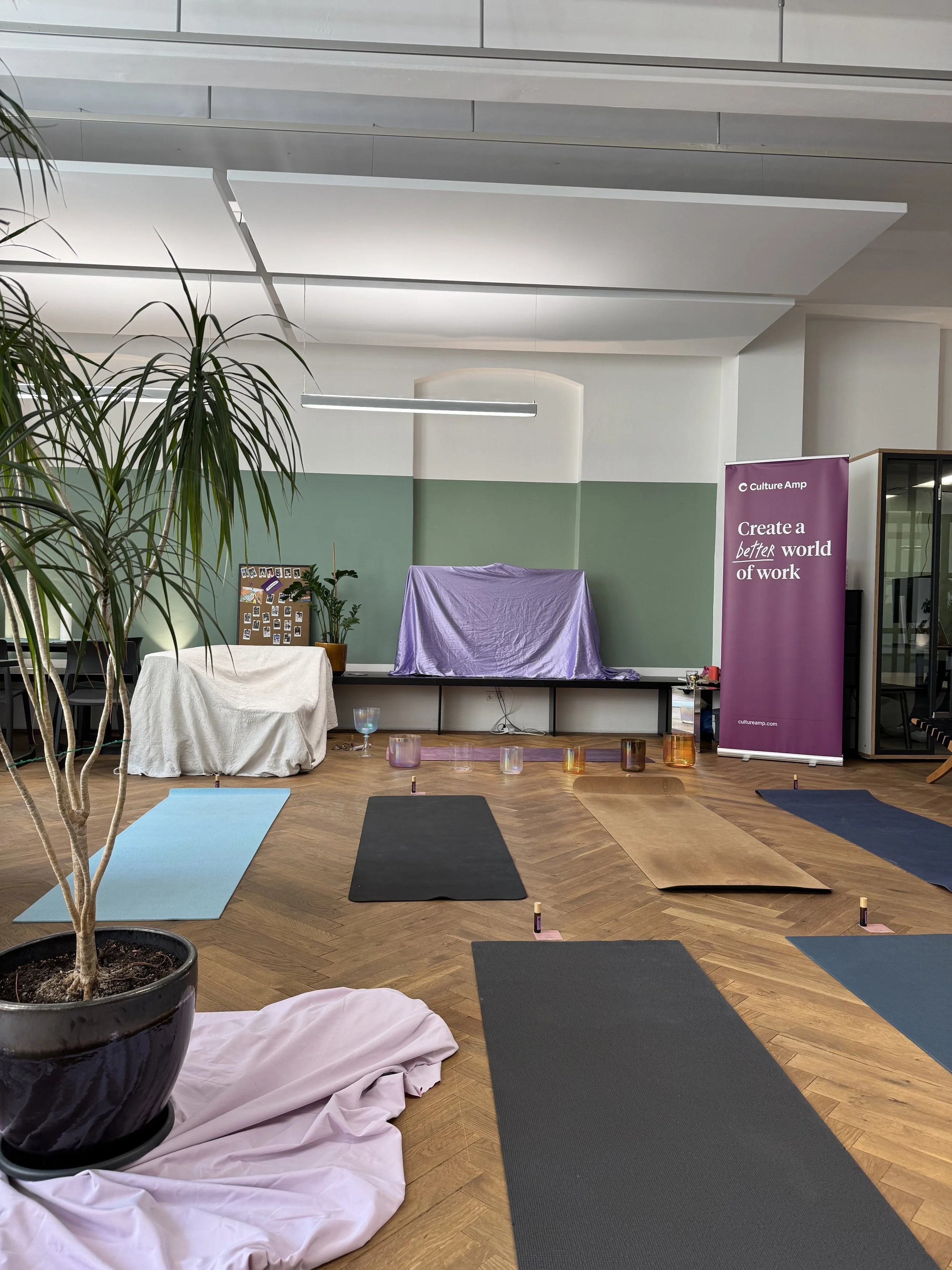 Office with mats laid out on wooden floor, potted plants, and a purple banner that reads 'Create a better world of work.'