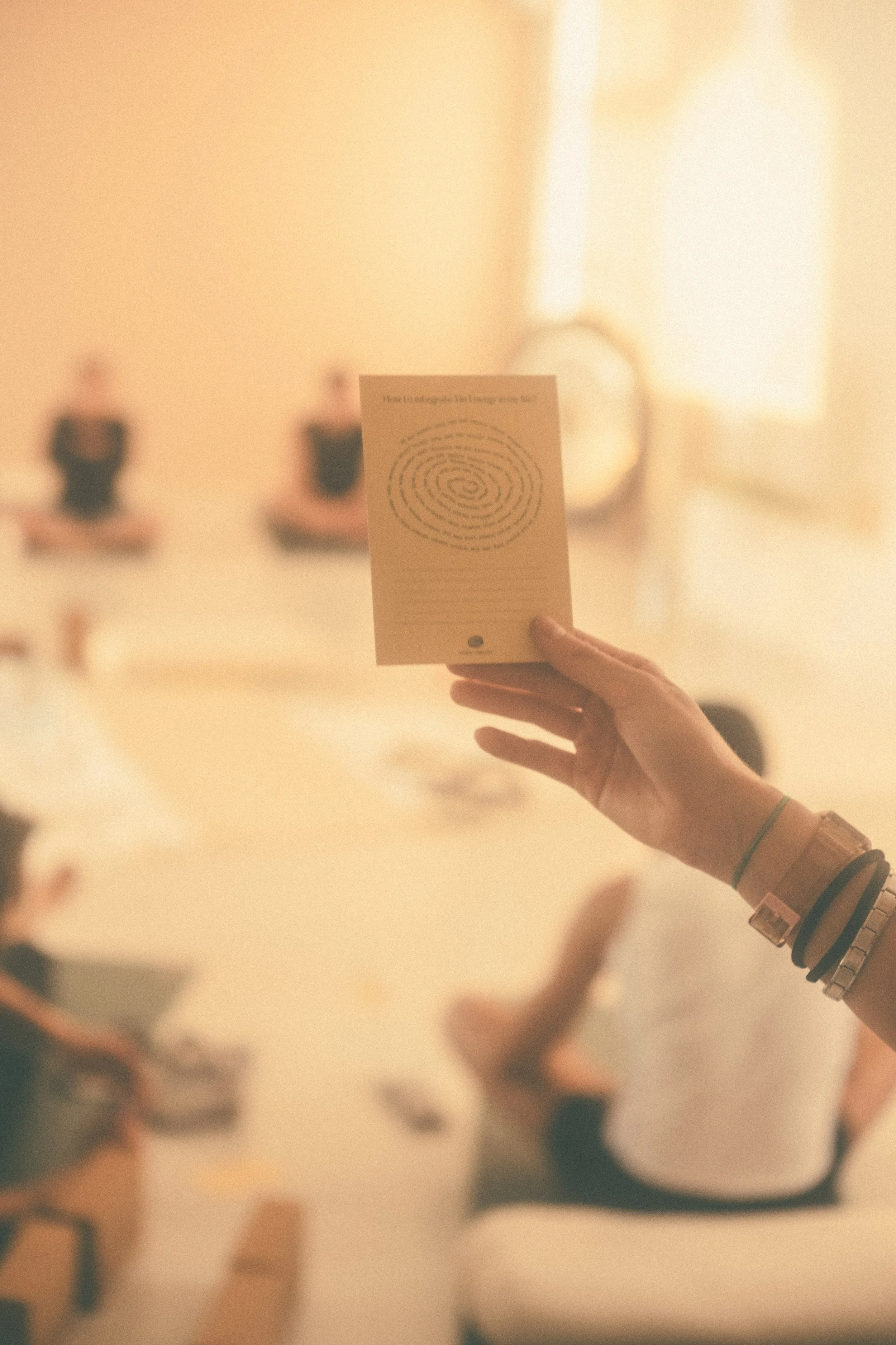 A person holding a card with a spiral maze printed on it, in a room with people sitting and using laptops.