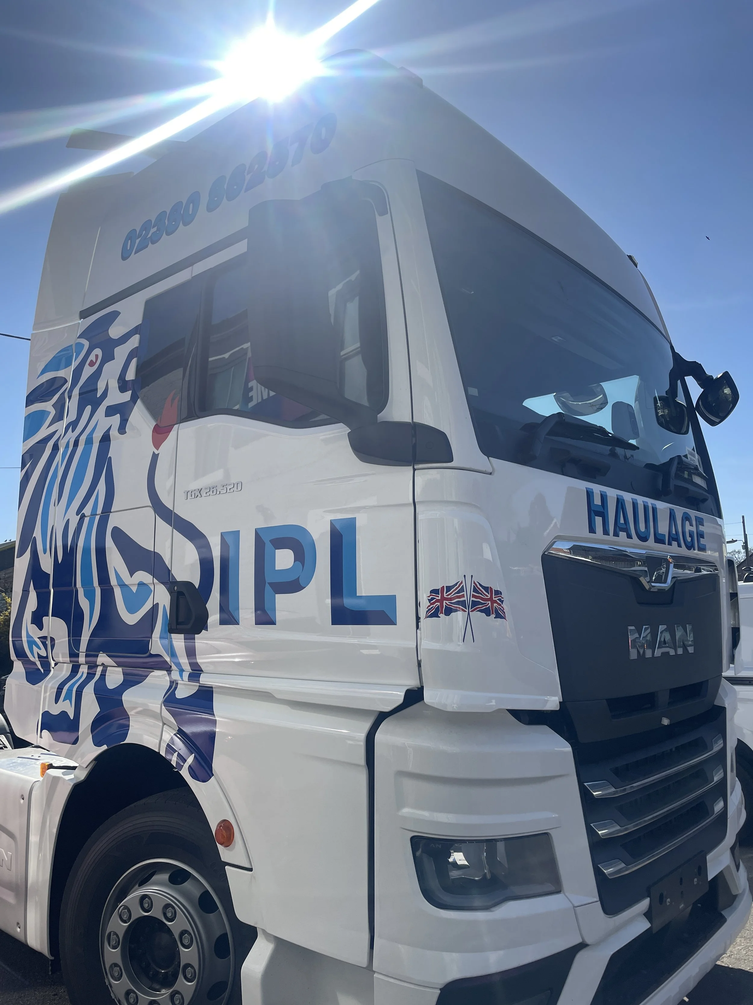 White truck with blue and red graphics and the words 'RPL HAULAGE' on the front and side, with a Union Jack flag decal on the side, parked outdoors under a bright sun.