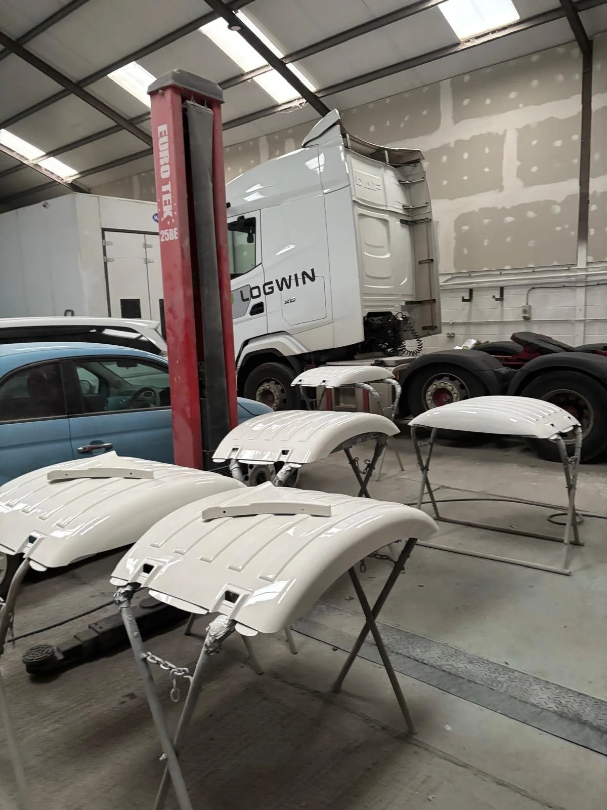 Painted white fenders or wheel covers on stands inside a garage or workshop, with a Ford truck and a car partially visible in the background.