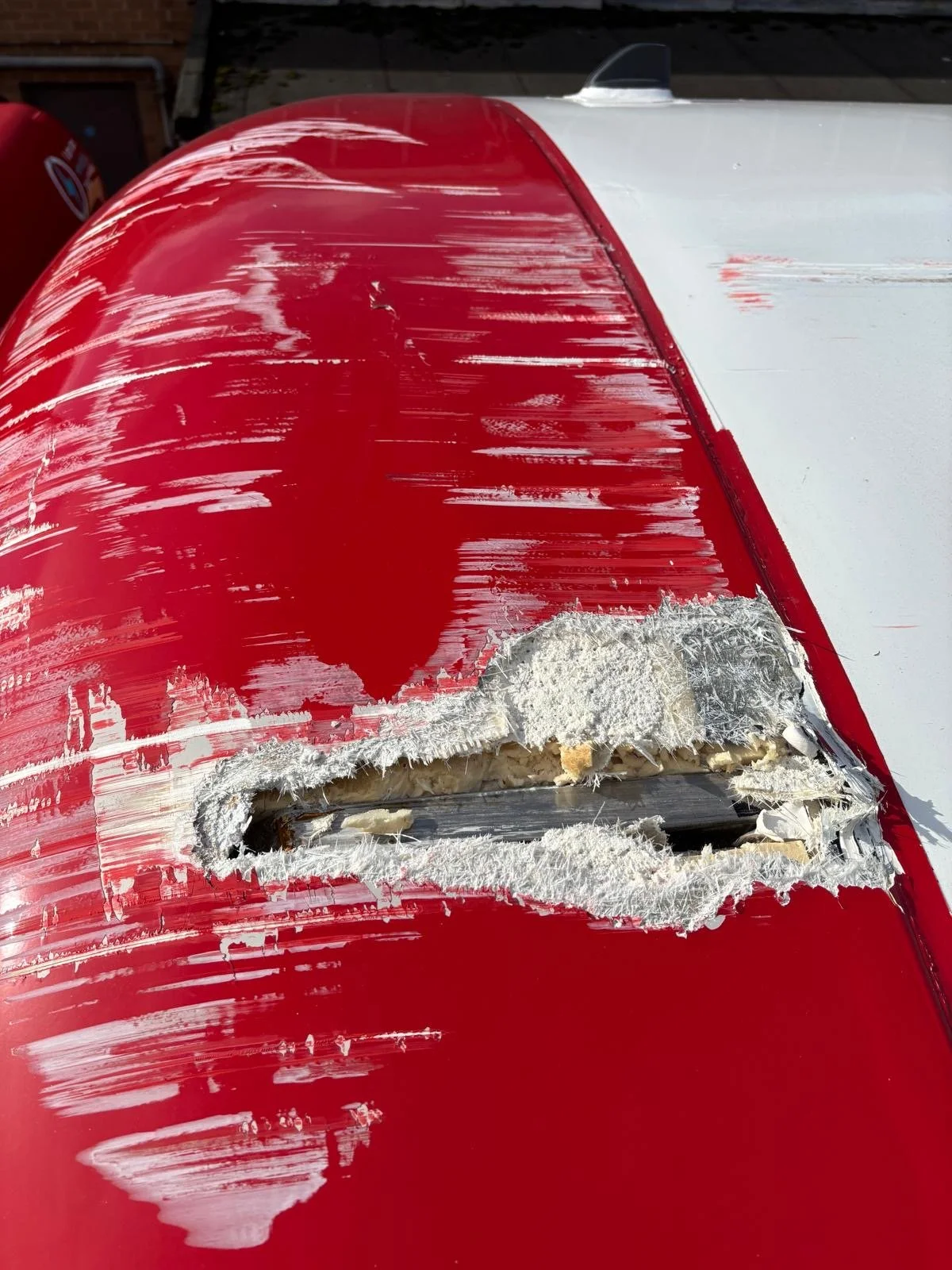 Close-up of a red and white surface with a large gouge, revealing insulation and metal underneath.