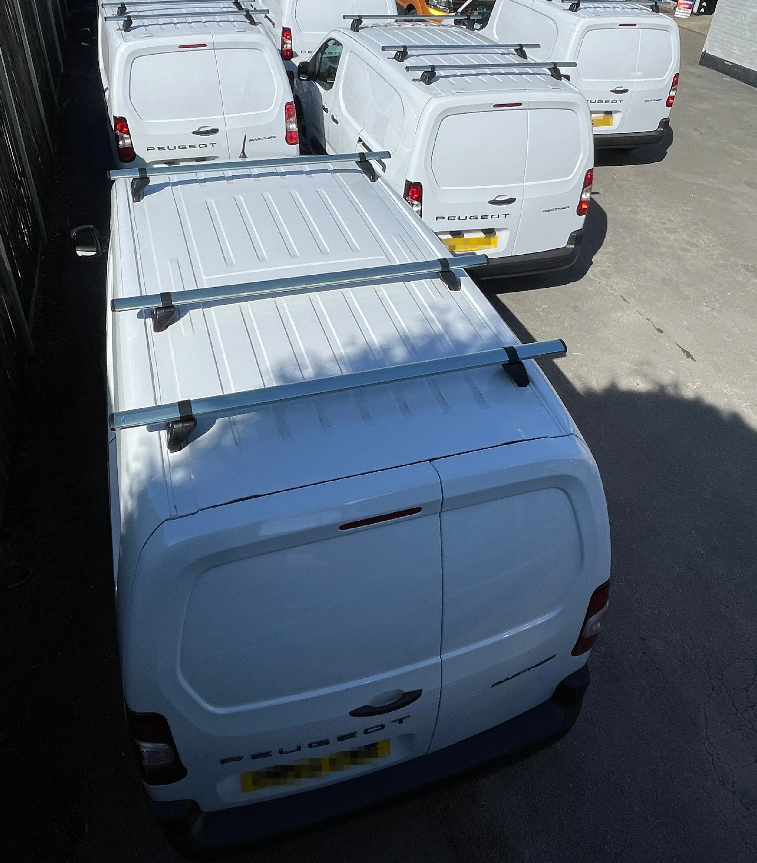 A white van with four roof racks parked among other white vans in a parking lot.