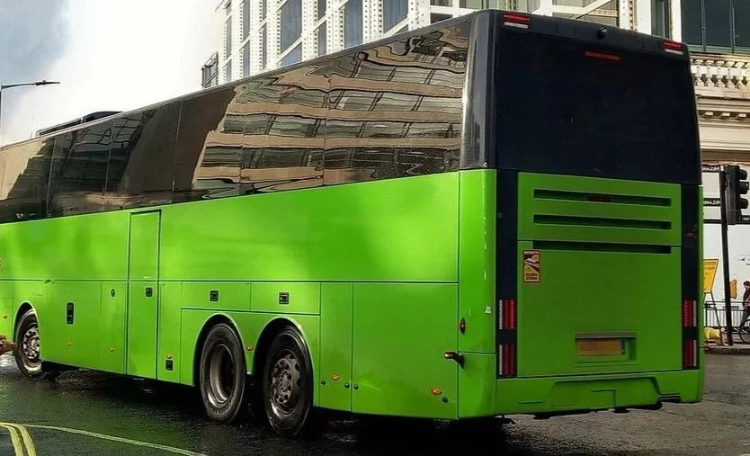 Green and black tour bus parked on city street, with buildings and street signs in background.