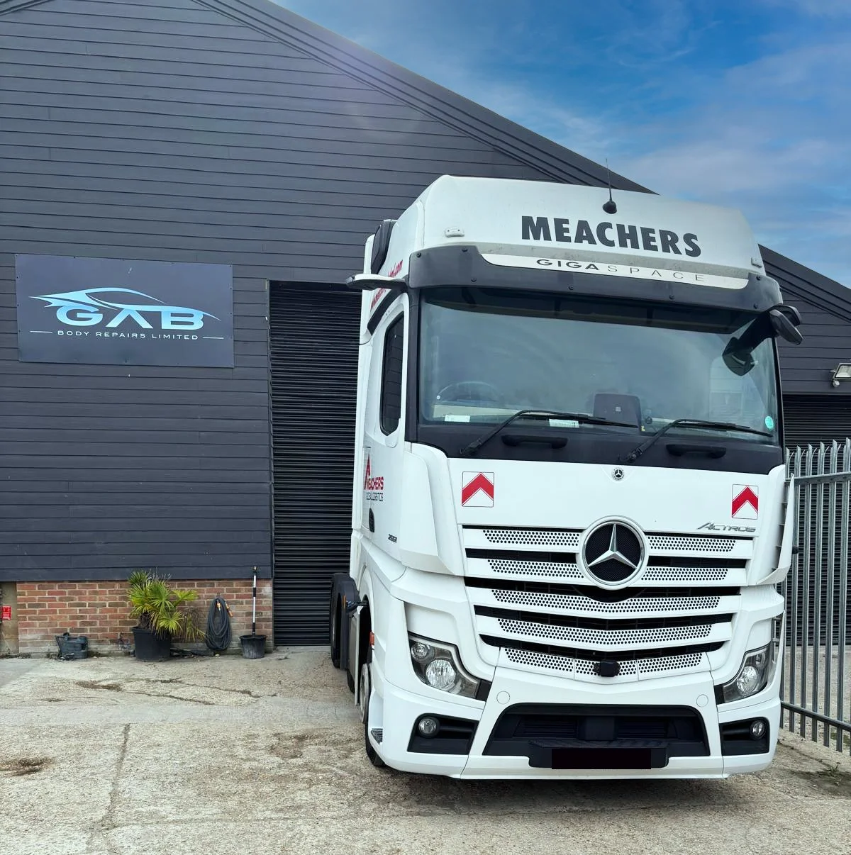 A white Mercedes-Benz truck with the company name 'MEACHERS' on the top, parked in front of a dark grey building with a sign that reads 'GAB Body Repairs Limited.'