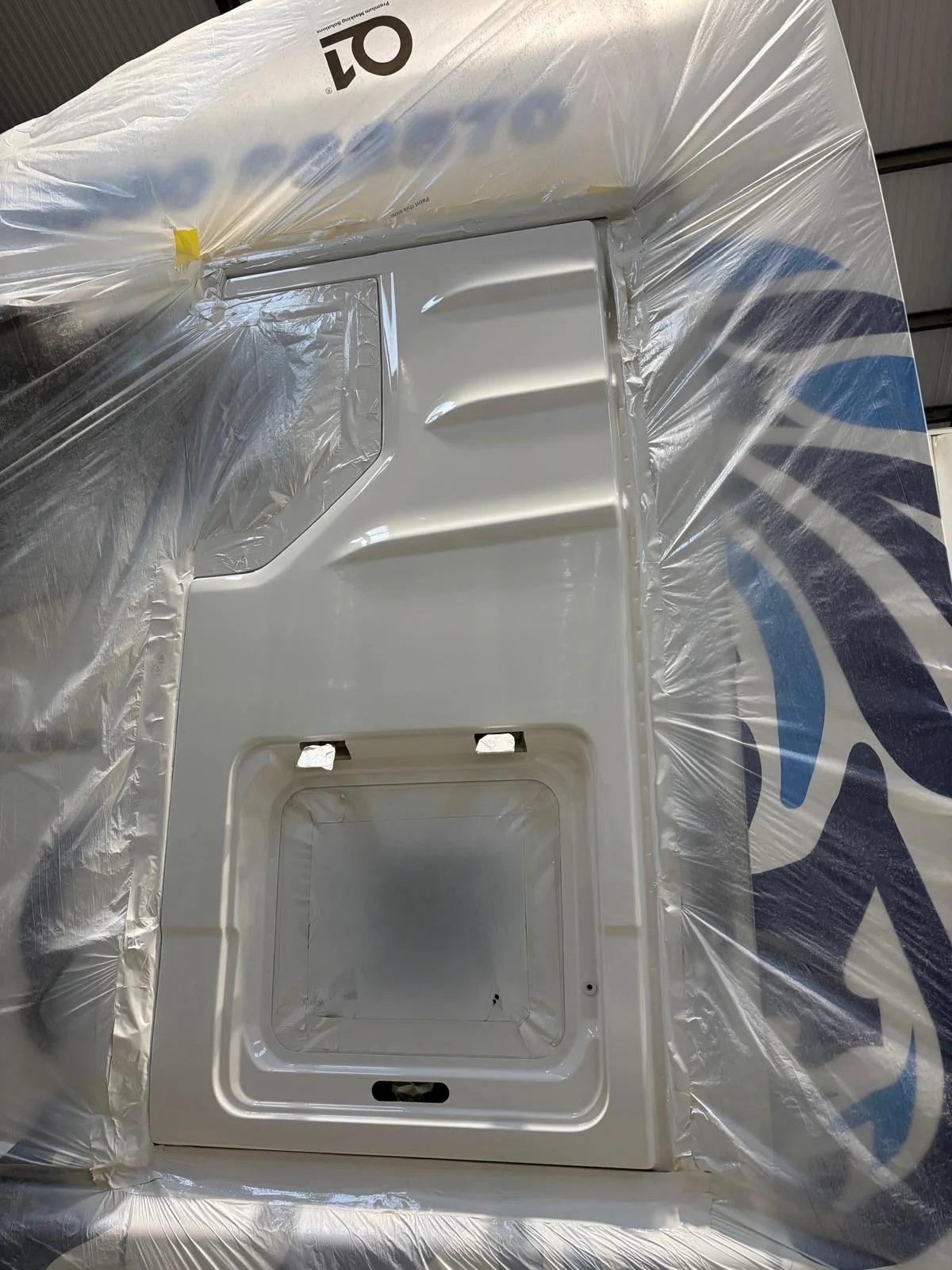 A white appliance, possibly an oven or microwave, surrounded by plastic and situated on a cardboard box.