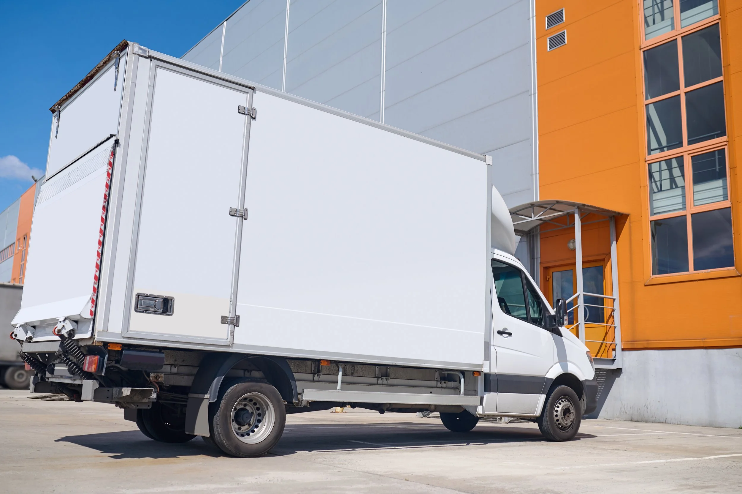White delivery truck parked in front of a modern orange and gray building.