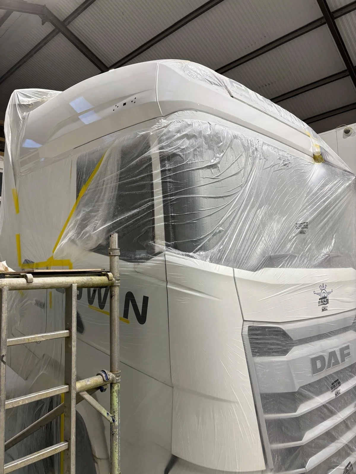 New white DAF semi-truck wrapped in protective plastic in a warehouse or workshop.