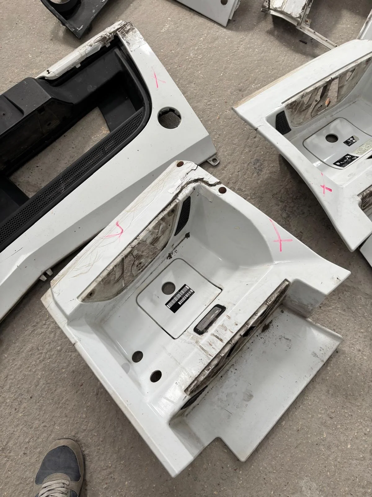 Three disassembled washing machine or appliance parts on a concrete floor, with visible dirt and scratches.