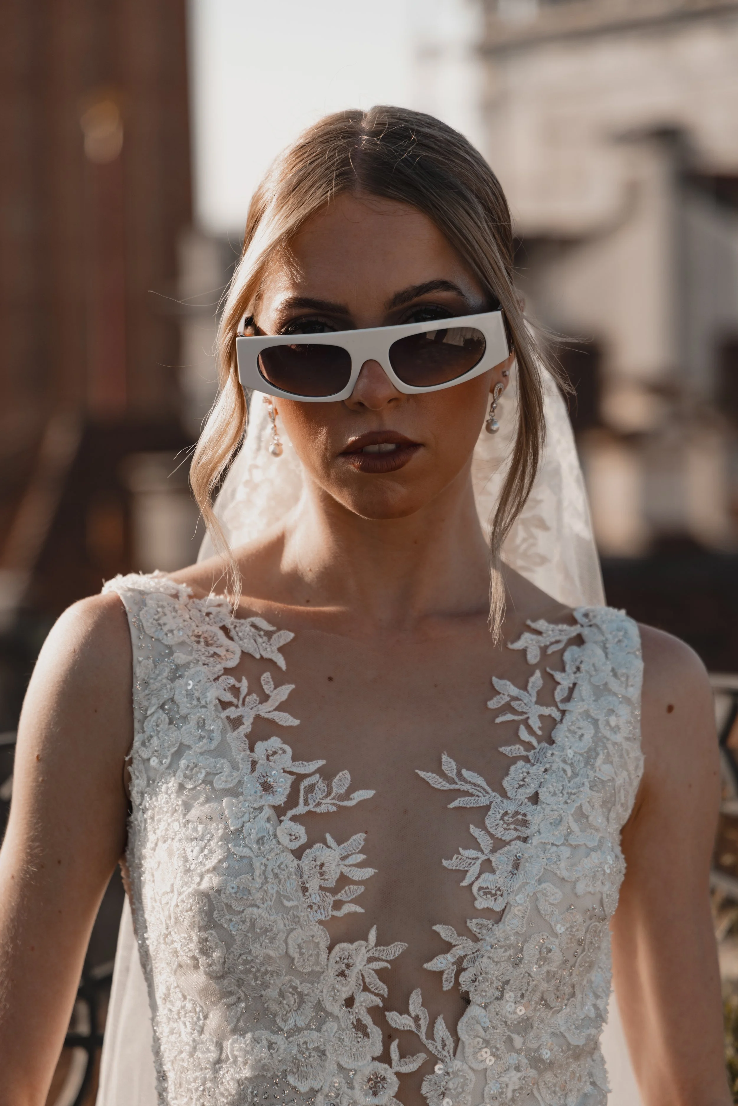 Close-up photo of a woman wearing a wedding dress and stylish sunglasses, outdoors during daytime.