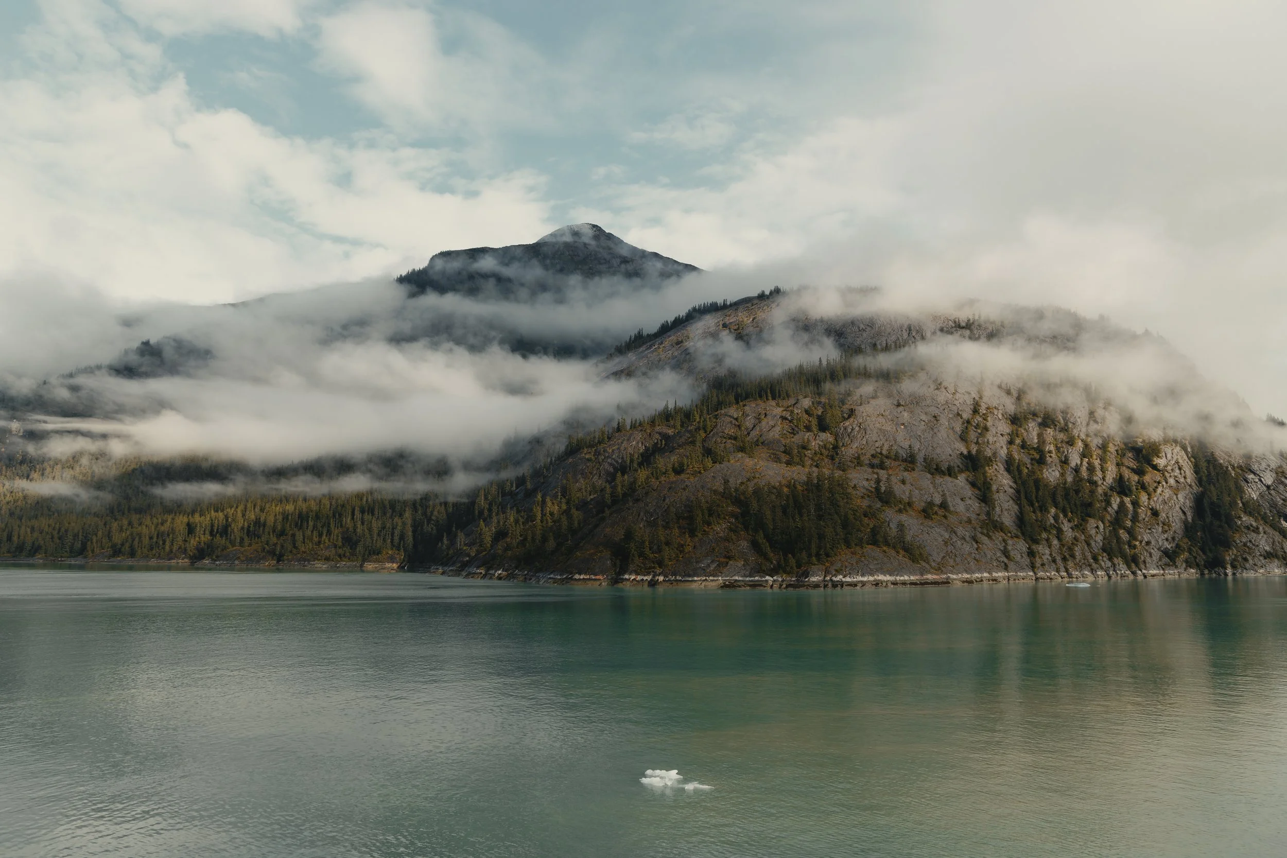 Mountain range partially covered with clouds, with a body of water in the foreground.