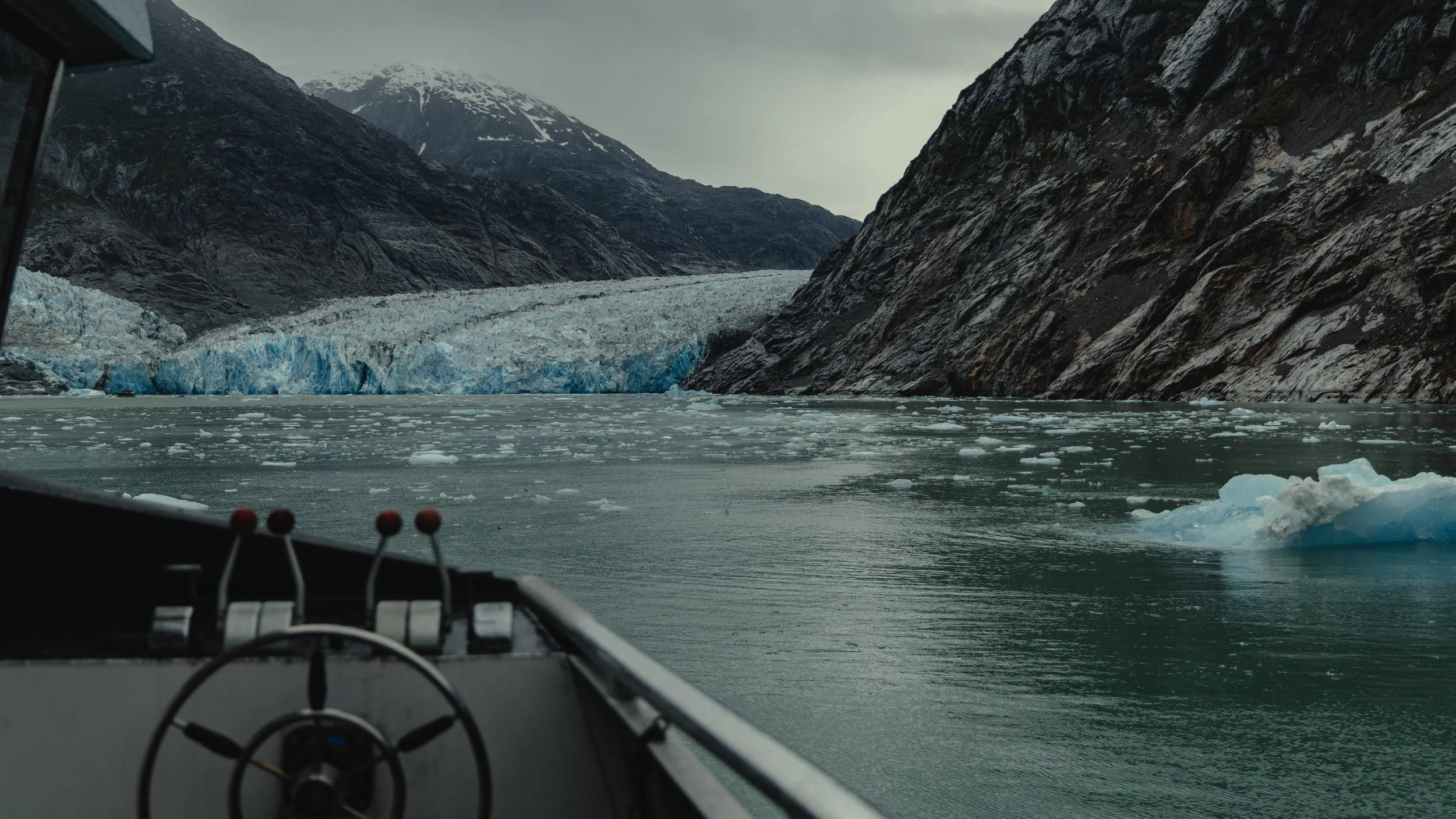 View from a boat showing a glacier melting into a body of water, surrounded by mountains, with ice floating on the water.