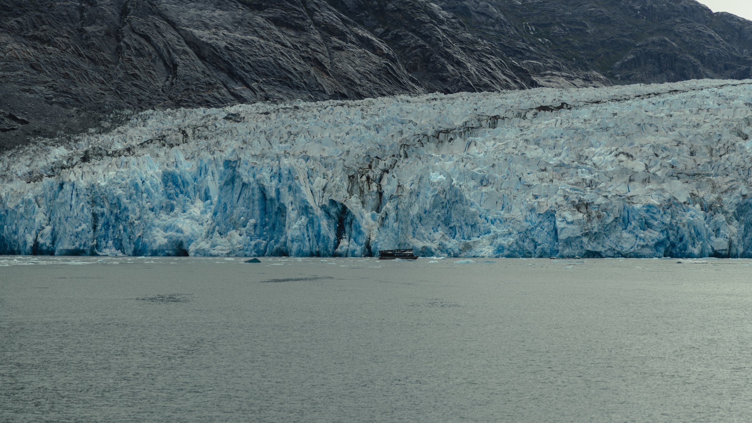 A glacier extending into a body of water with a boat nearby for scale.