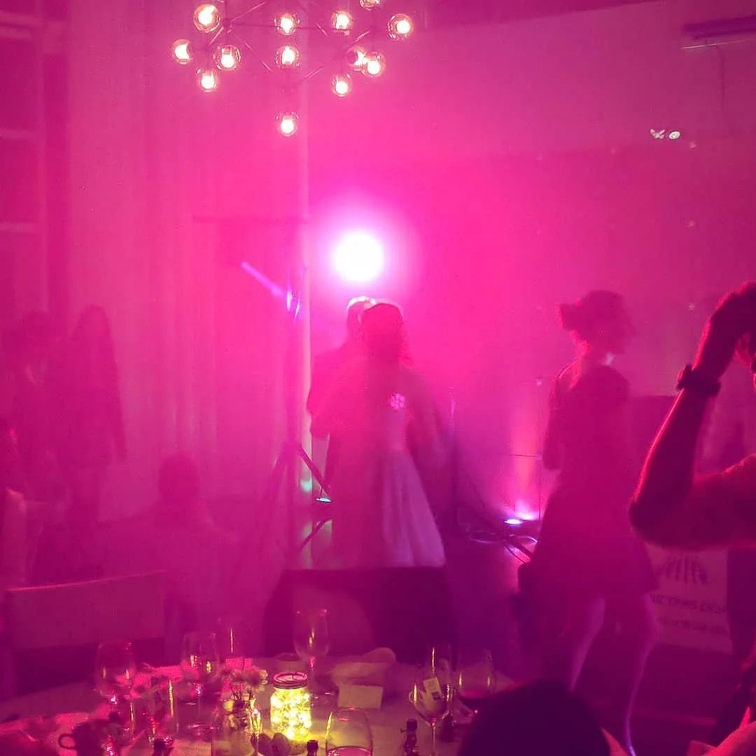 People dancing at a party with pink lighting and a chandelier overhead.