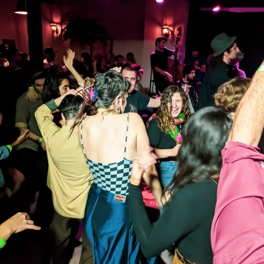 People dancing and socializing at a lively party with a live band performing on stage in the background.