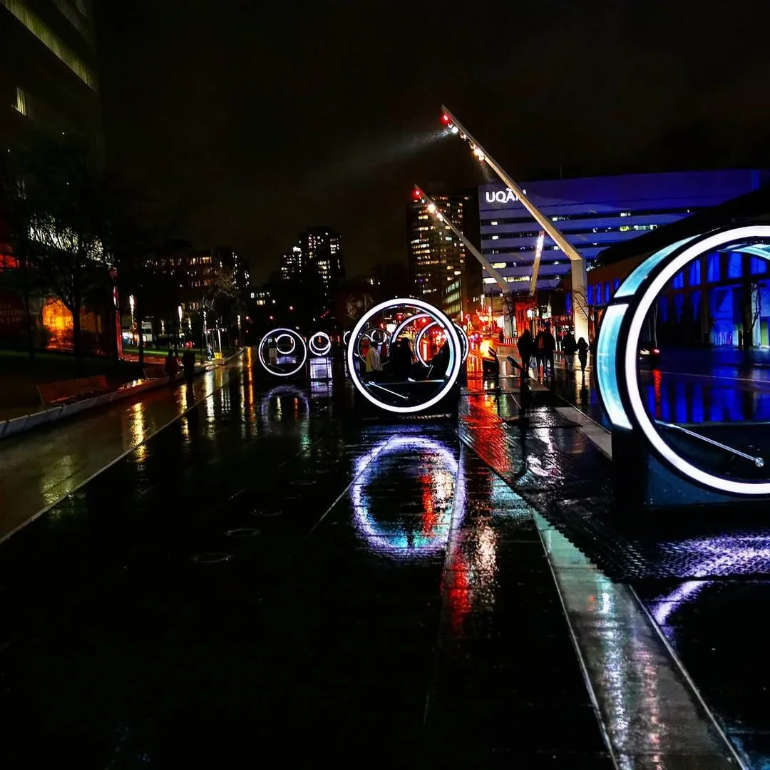 Nighttime city street with illuminated circular art installations and reflections on wet pavement.