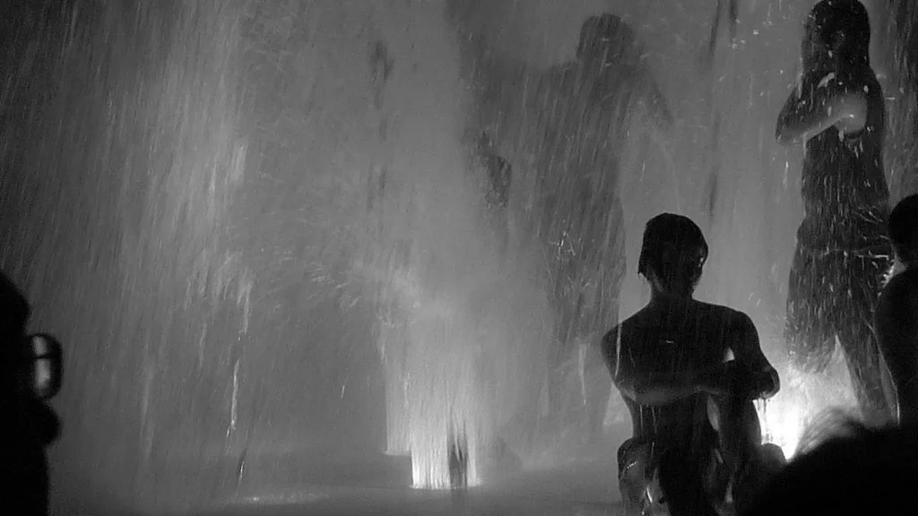 People standing in the rain at night, with one person sitting on the ground and two others standing in the background.