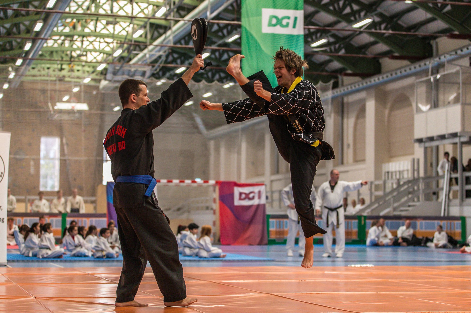 Martial artists practicing martial arts in a gymnasium for a competition or demonstration, with everyone in martial arts uniforms.