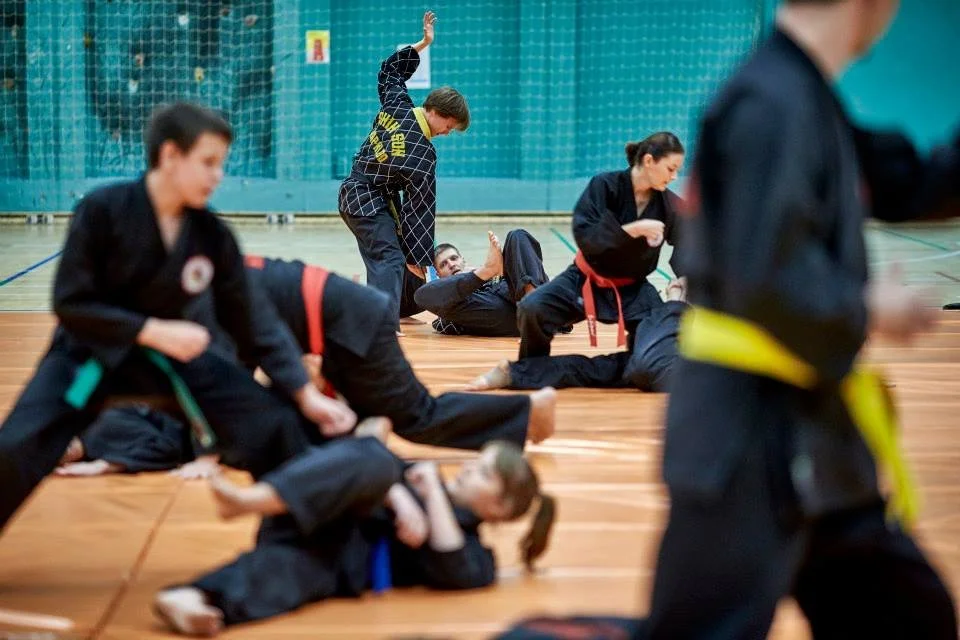Martial arts class practicing grappling and self-defense techniques in a gymnasium.