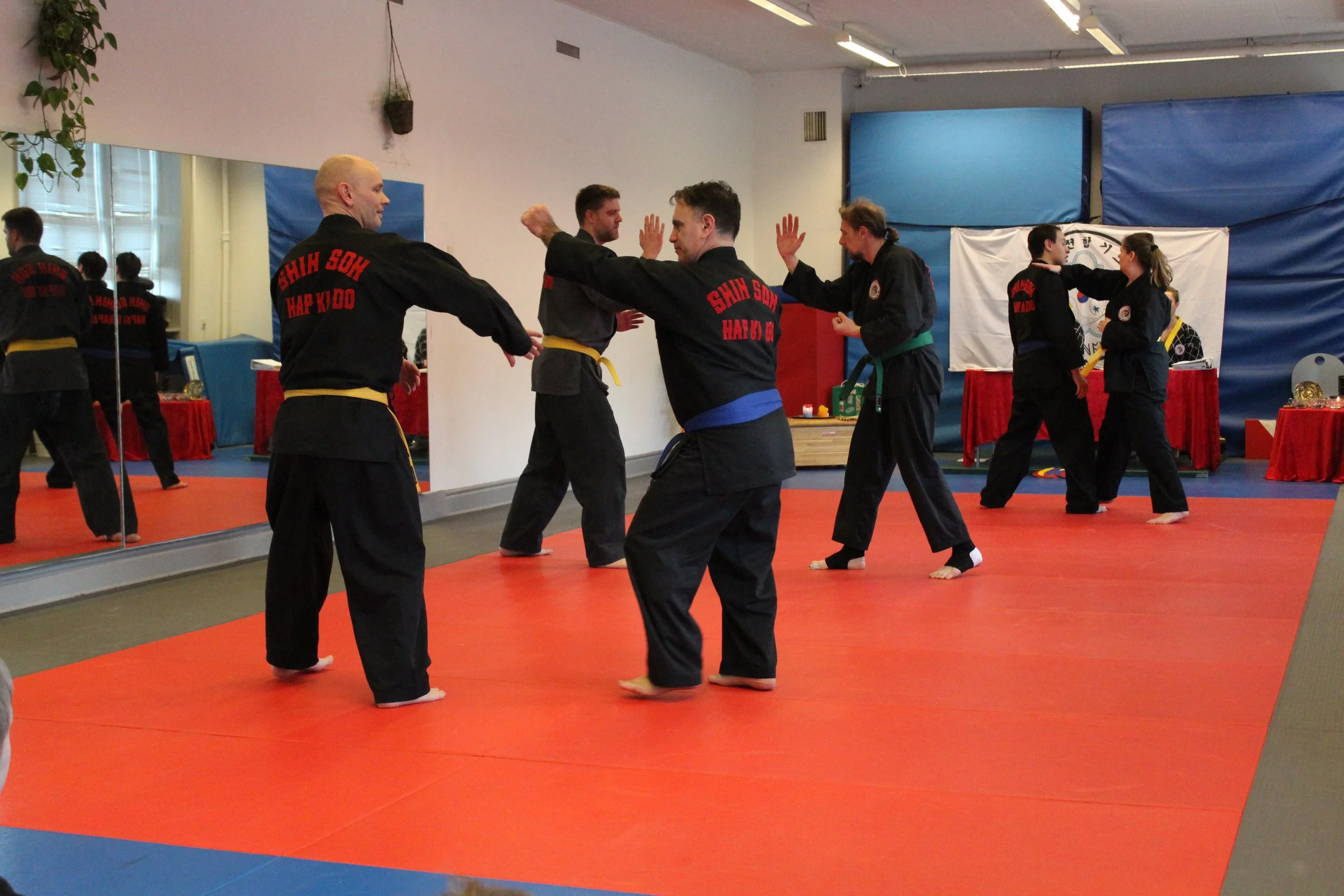 Martial arts students practicing techniques in a dojo with mirrors on the wall.
