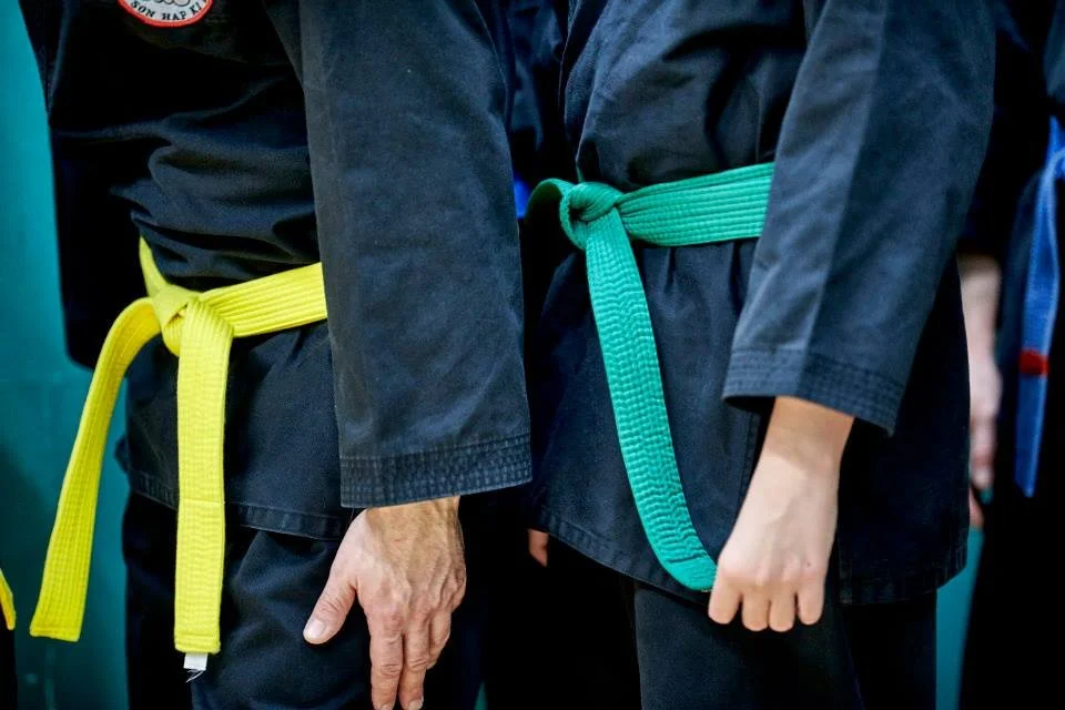 Close-up of two martial artists wearing black gis with green and yellow belts, standing side by side.