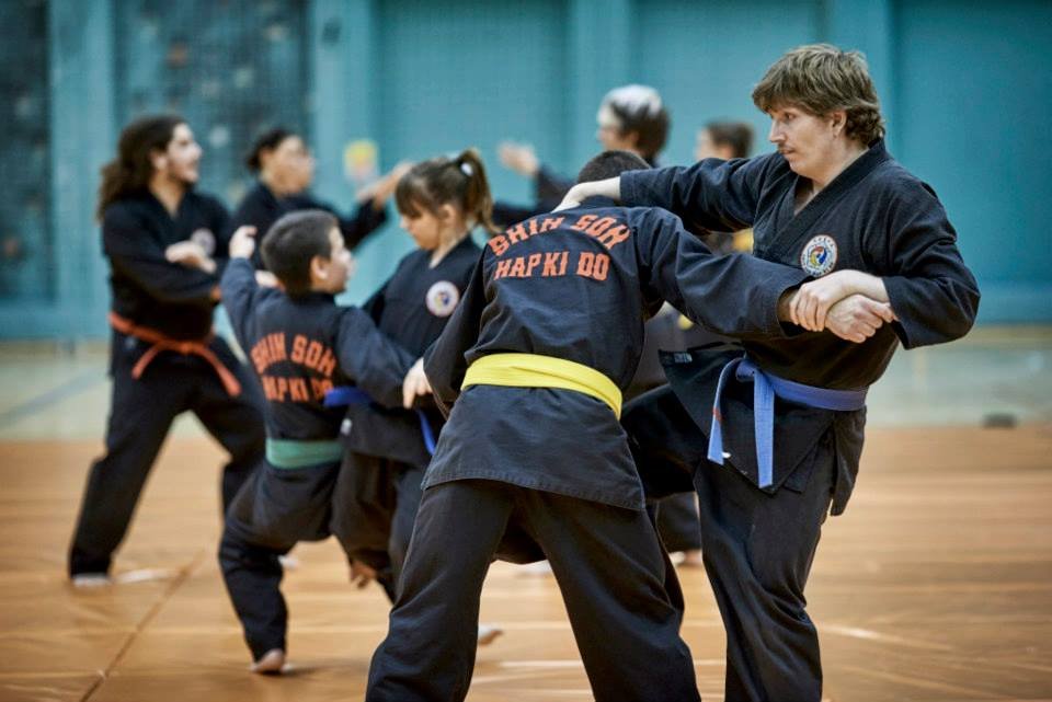 Martial arts class with children practicing techniques with an instructor in a gymnasium.