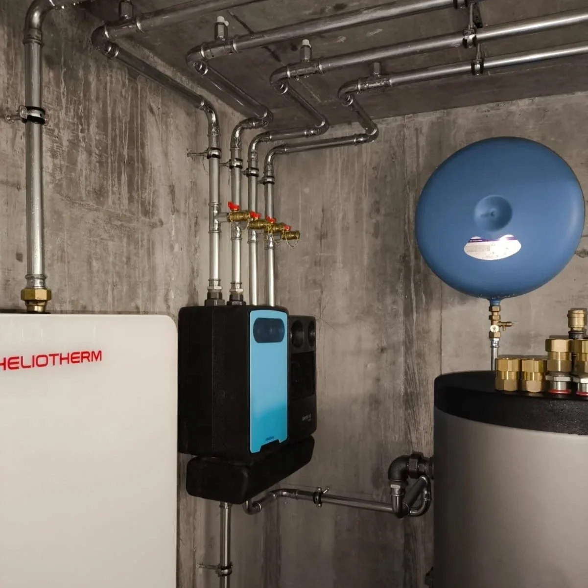 Système de plomberie avec réservoir d'eau bleuté, échangeur de chaleur, conduites en métal, et équipement de chauffage ou de traitement d'eau, dans une pièce de bâtiment.