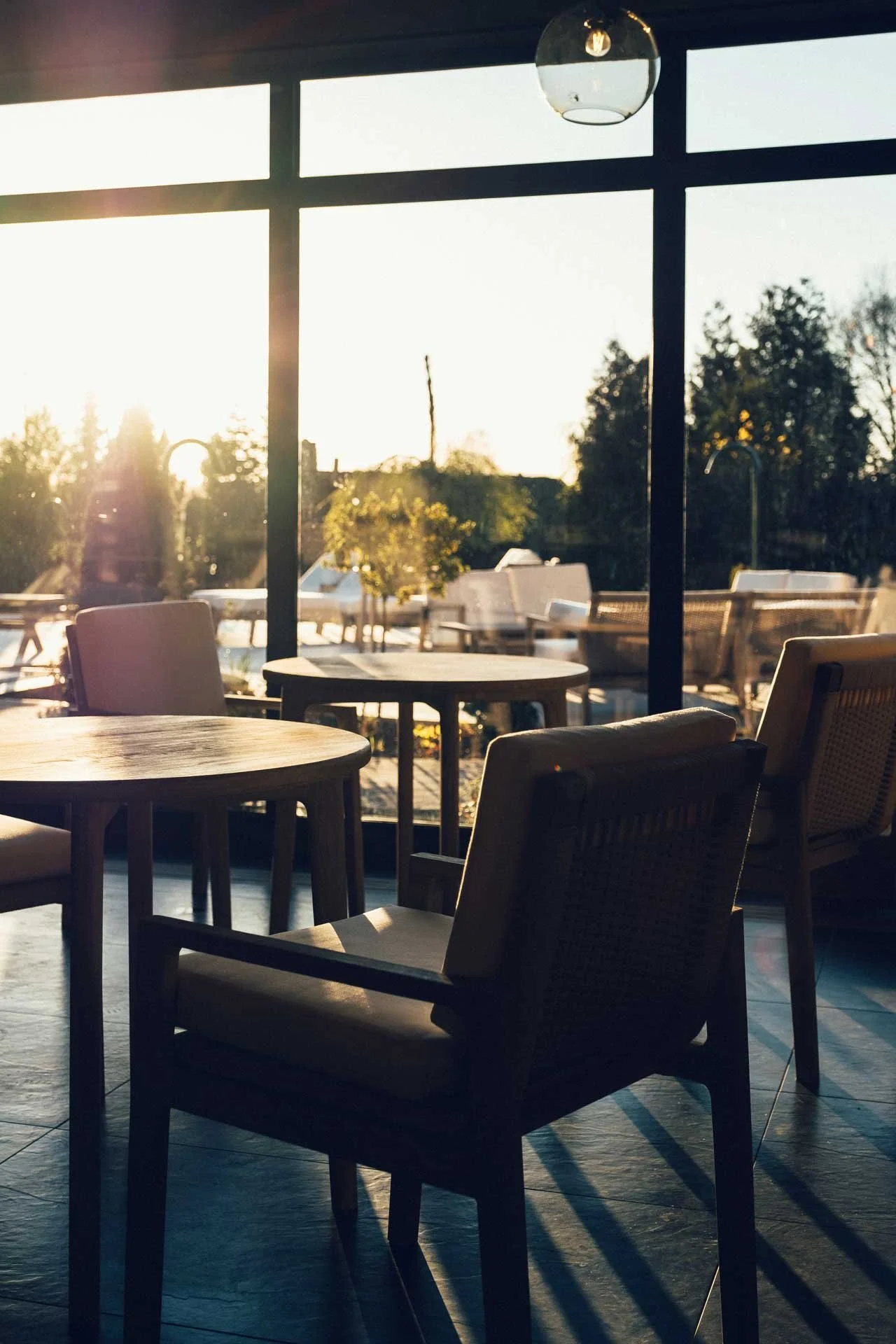 Ästad Vingård - Bord och stolar vid en glasvägg - ser ut över pool och grönska.jpg