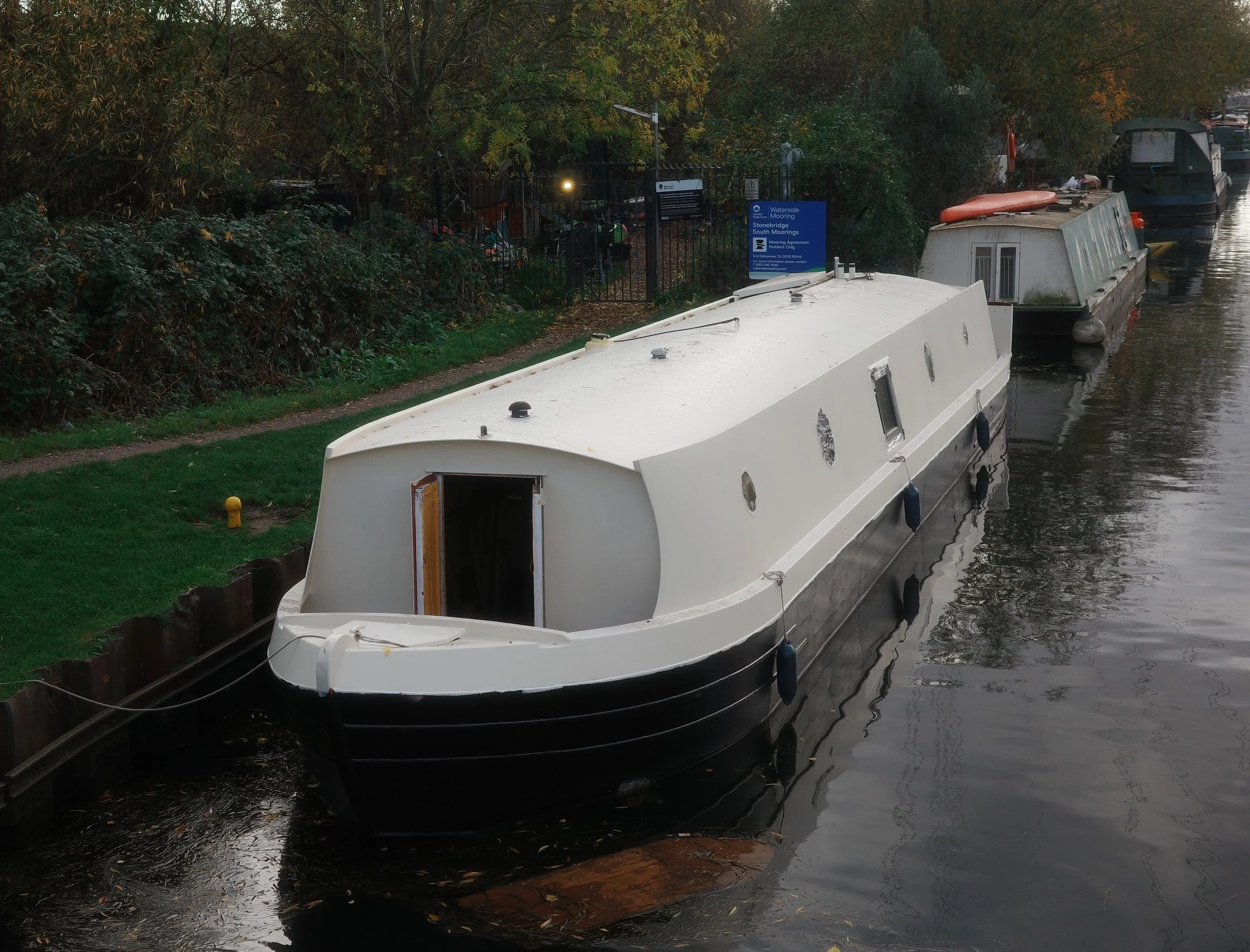 The sauna on a canal boat docked on a calm river, with solar panels on the roof and large round windows on the side looking into the sauna