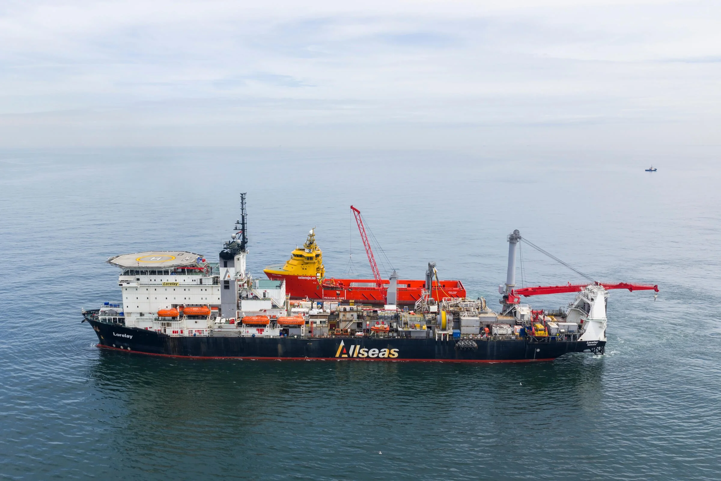 A large black and white offshore supply vessel named Lorelay on calm ocean water with cranes, equipment, and a smaller red and yellow rescue boat on deck.