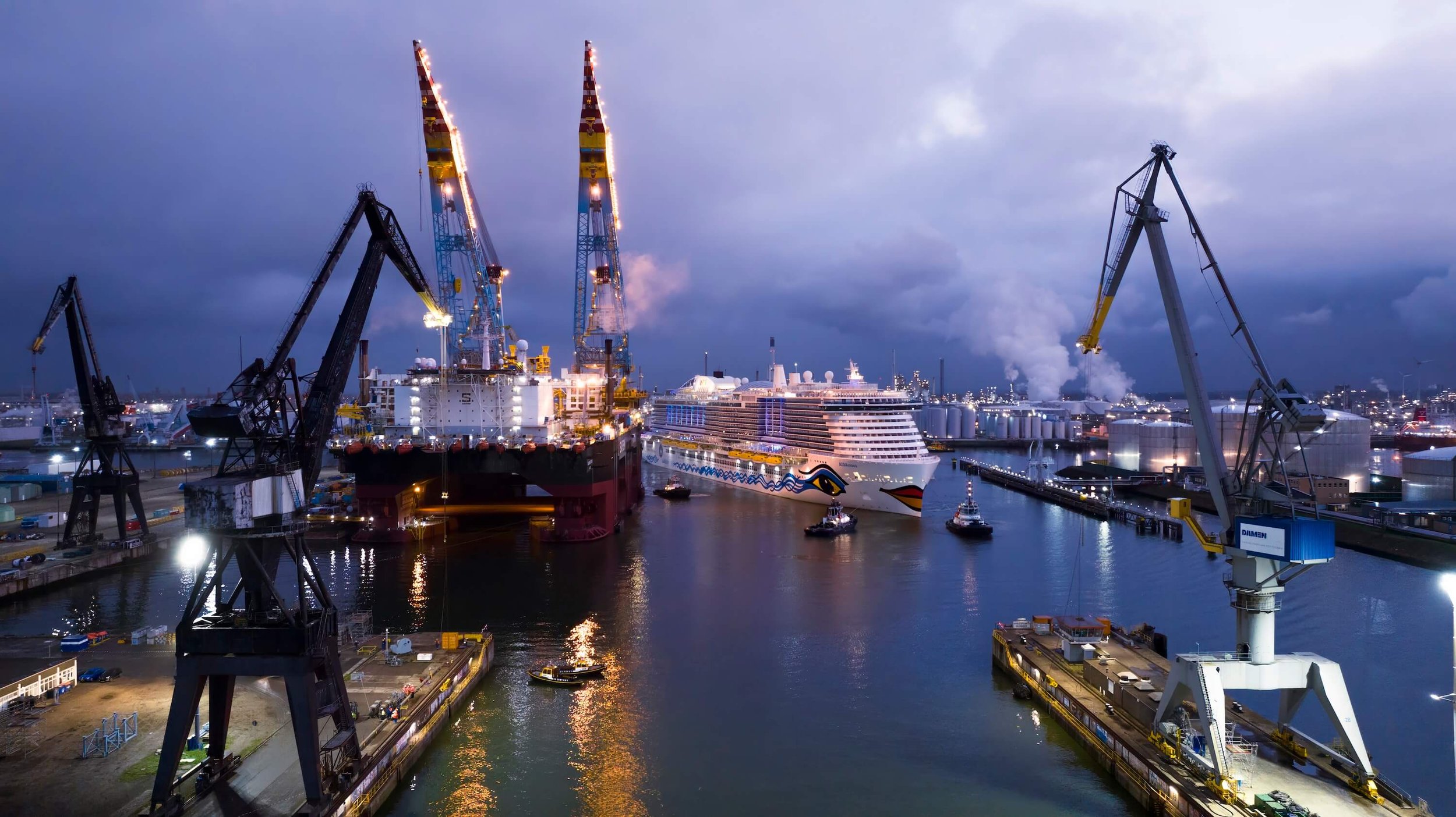 Night view of a busy port with cargo cranes, a cruise ship, and a busy shipping yard.