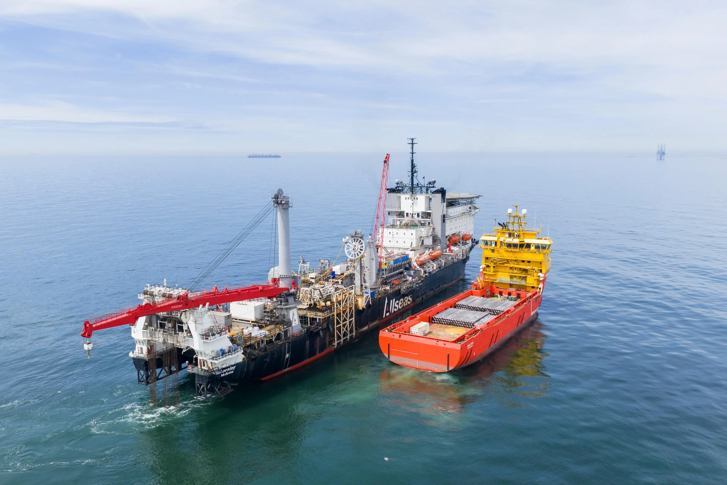 An oil supply ship in the ocean with a smaller support vessel alongside, under a cloudy sky.