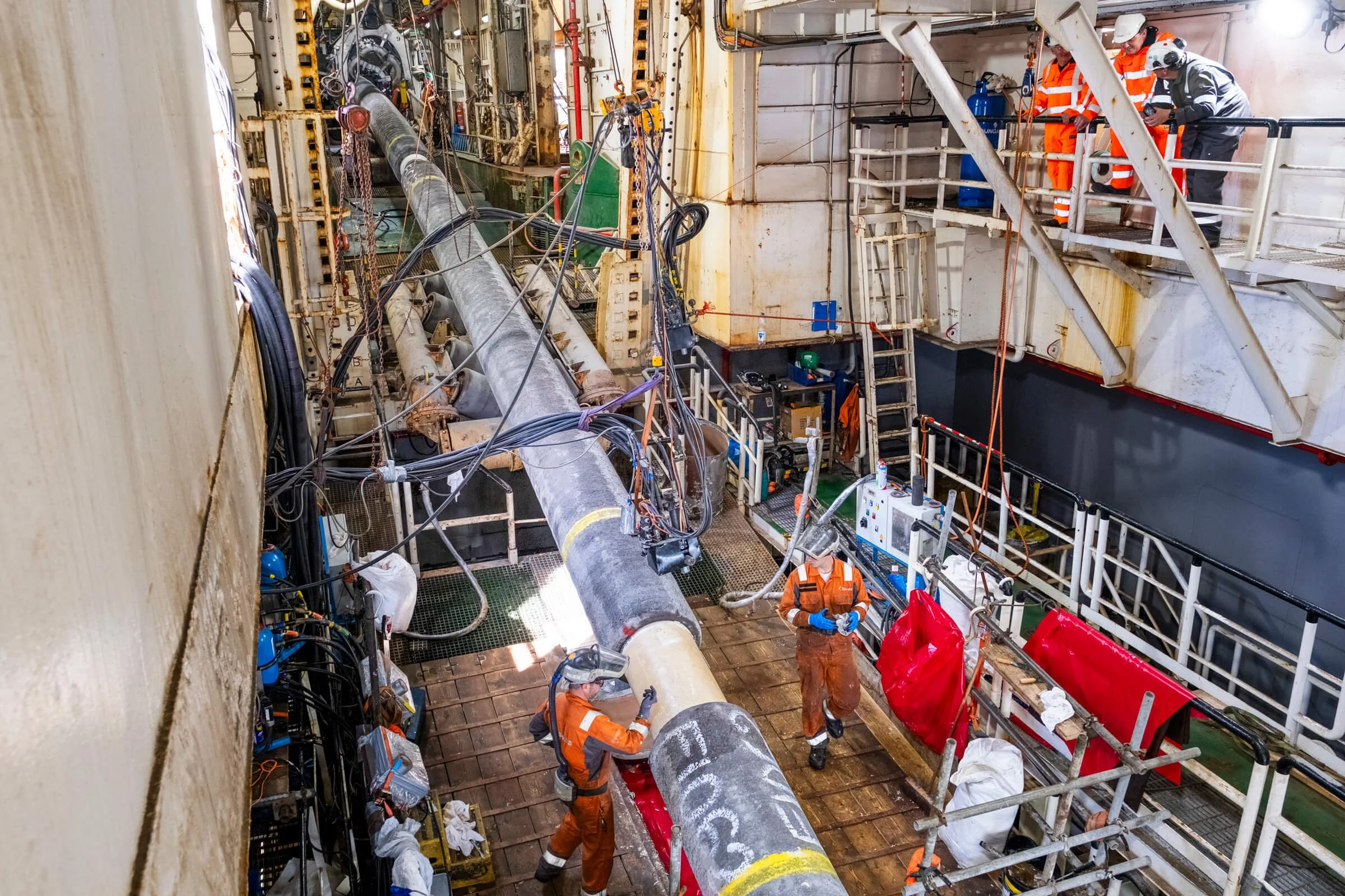 Workers in safety gear working on a large industrial pipe on offshore oil or gas platform.