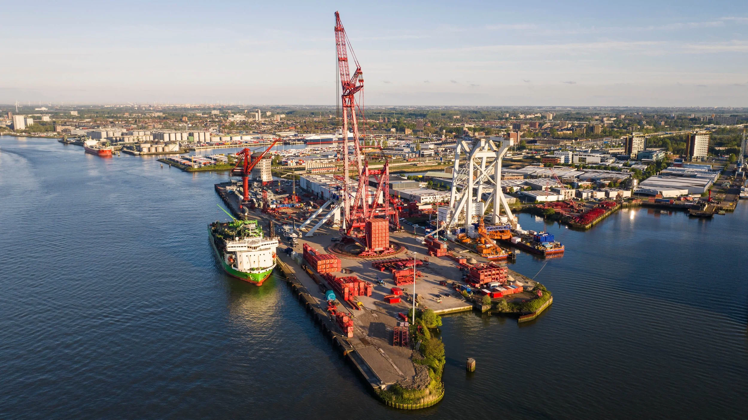 Aerial view of a busy shipyard with large cranes, ships, containers, and industrial buildings along the water.