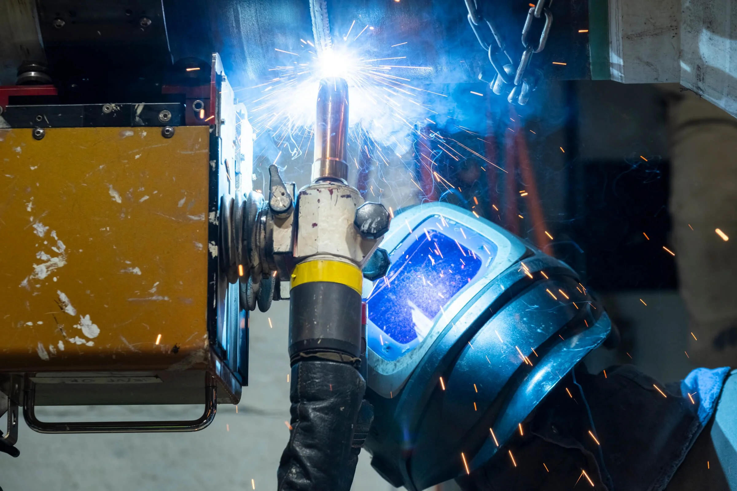 A person welding metal with a bright arc and sparks flying in a workshop.